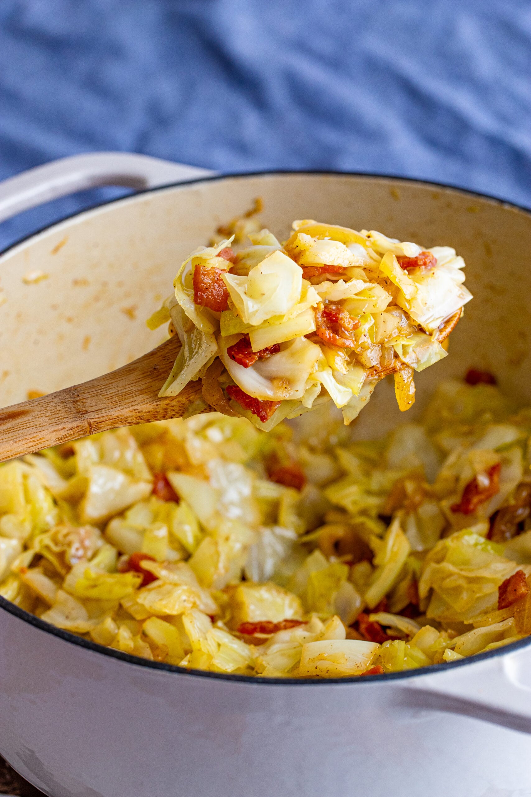 Fried cabbage being removed with a wooden spoon from a large Dutch oven. 