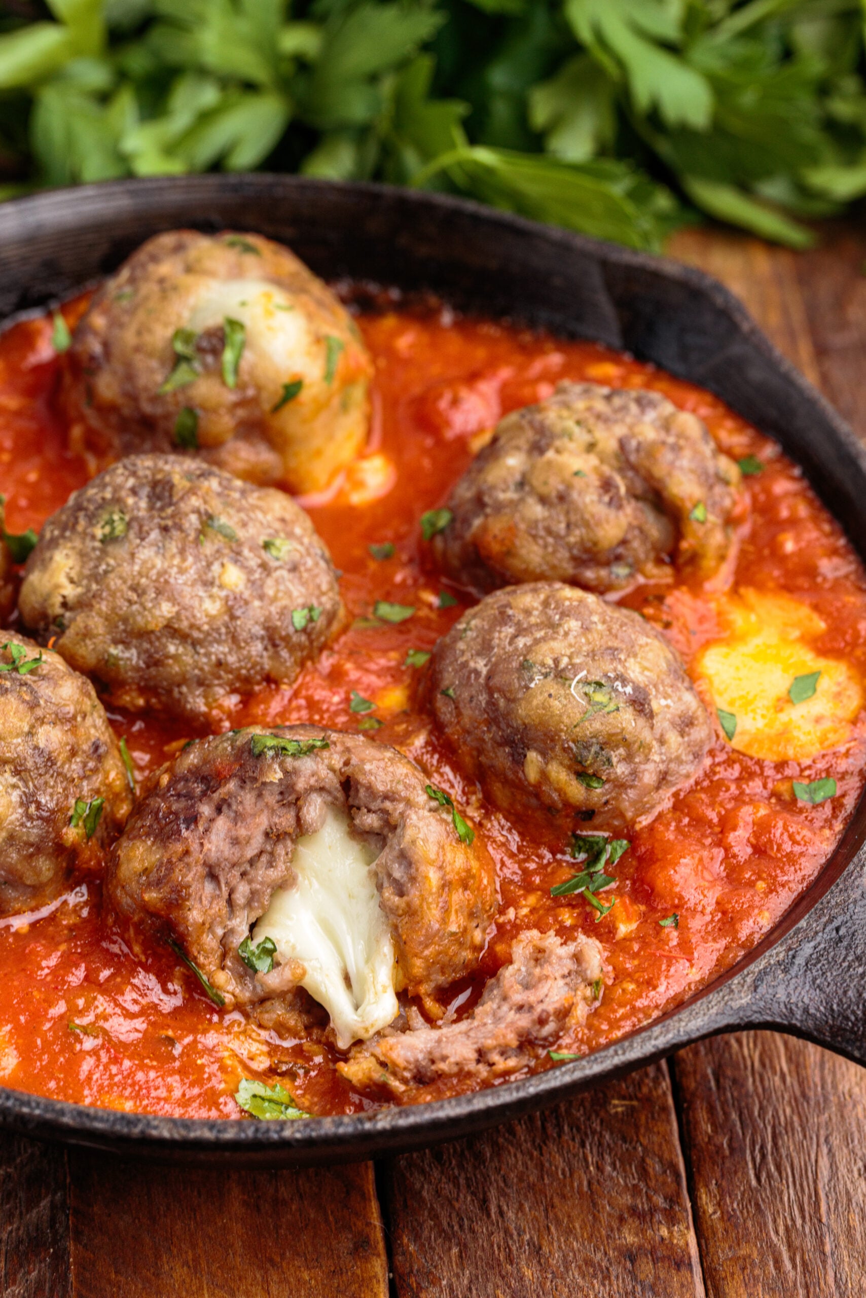 Overhead view of Mozzarella Stuffed Meatballs in a cast iron skillet with one meatball cut open by a silver fork.