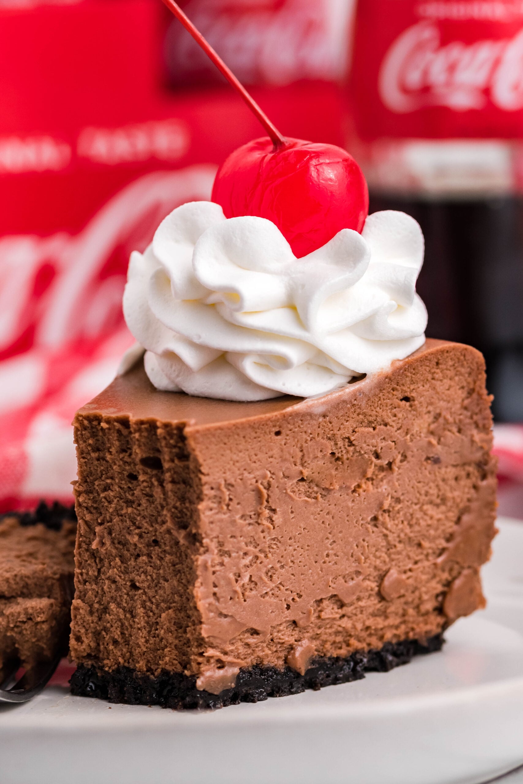 Coca-Cola Cheesecake slice on a white plate topped with whipped cream and a cherry