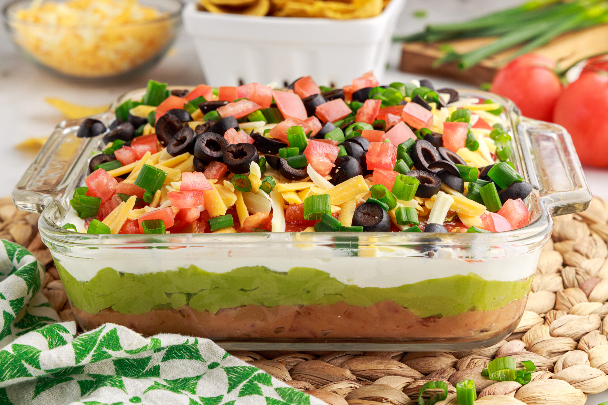 7 layer dip in a clear baking dish with chips and cheese in the background