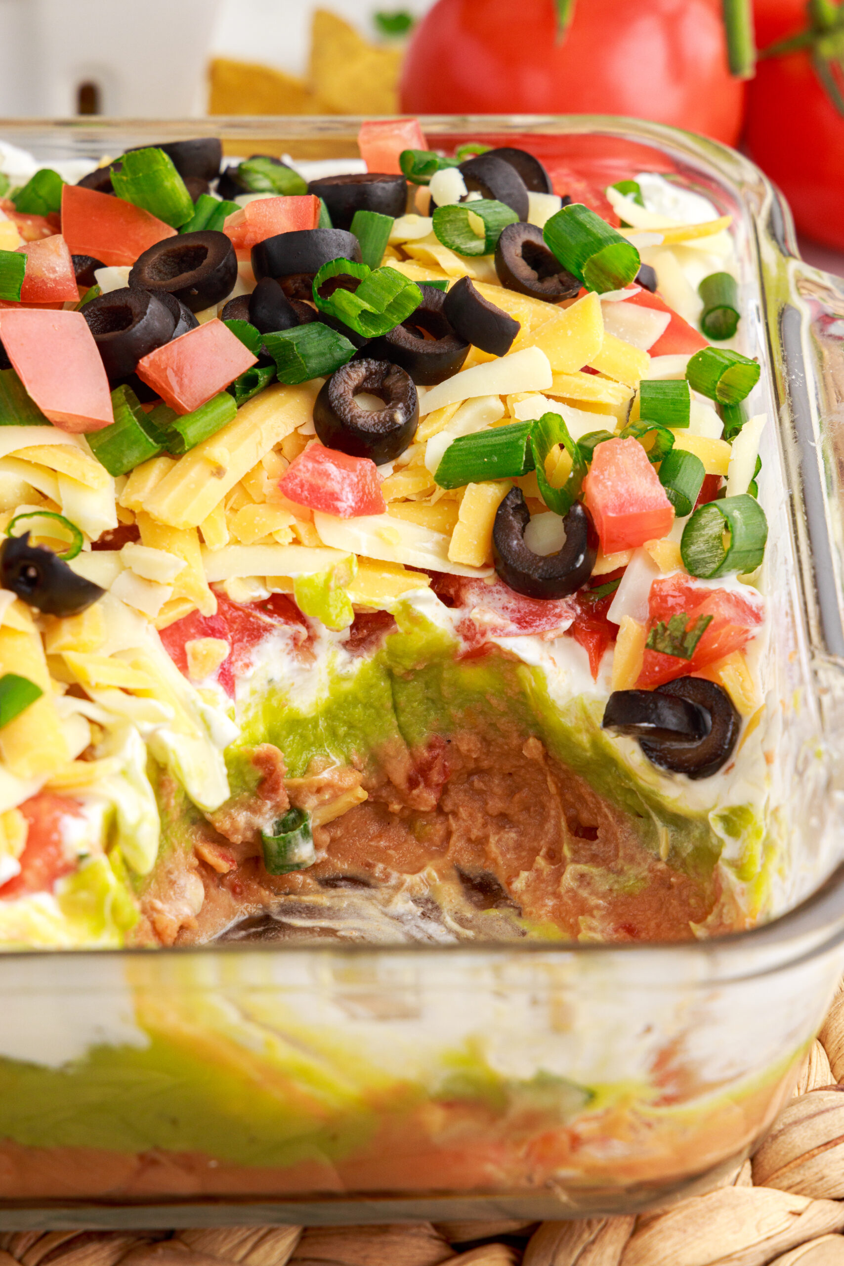 Close up view of 7-Layer Dip in a clear baking dish with a serving removed.