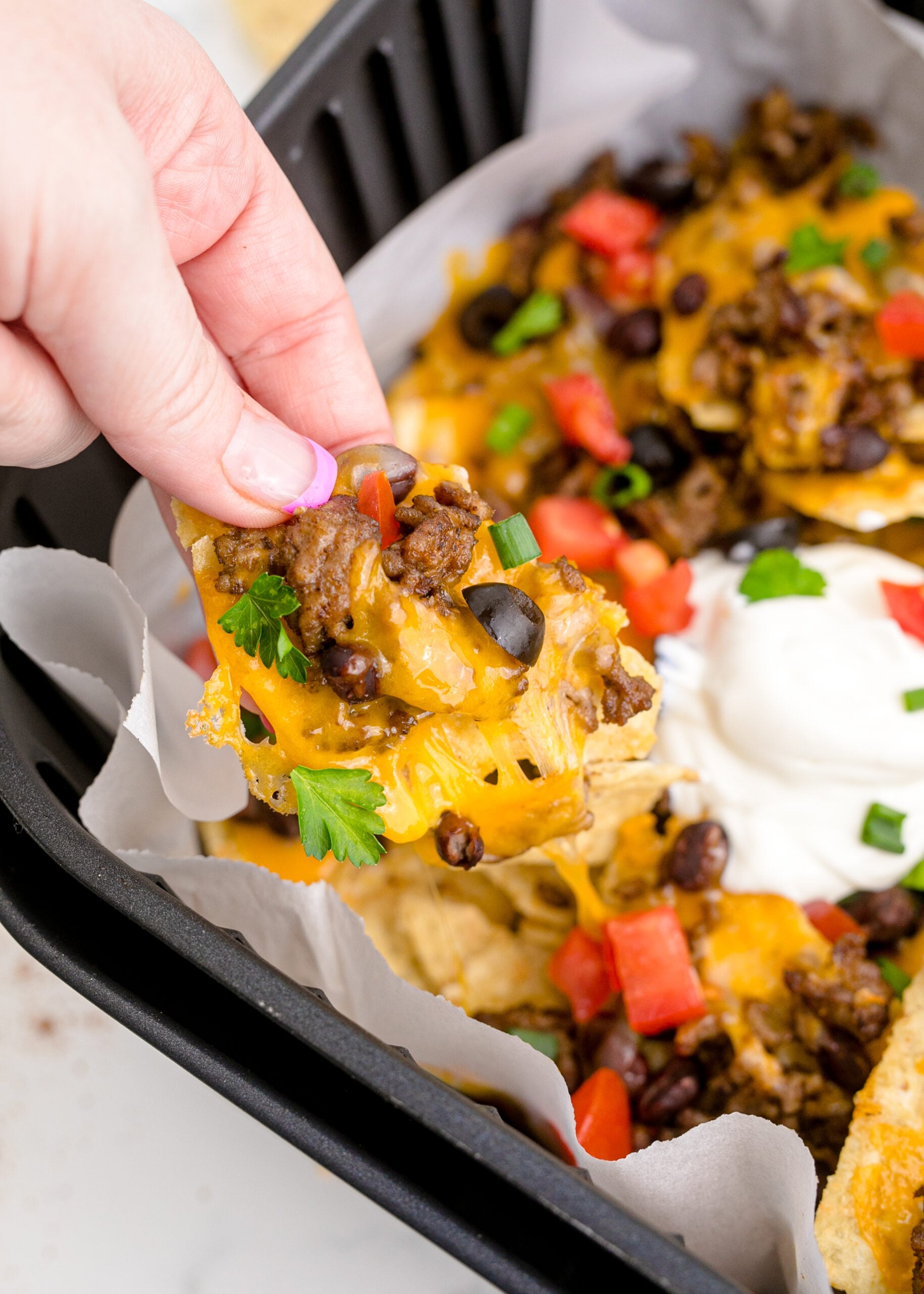 Up close view of Air Fryer Nachos in an air fryer basket and one nacho being held.