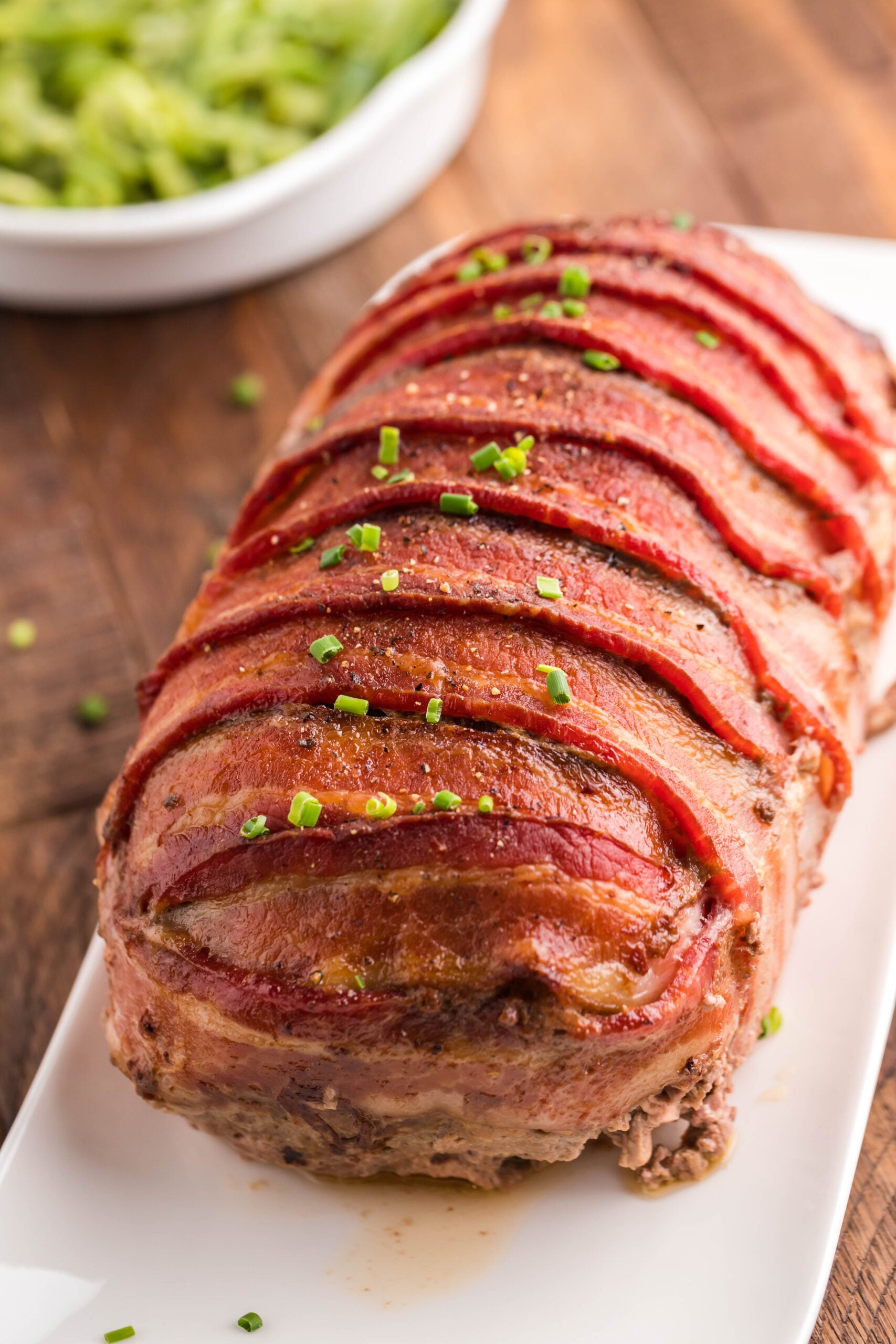 View of Bacon Wrapped Meatloaf on a white serving dish.