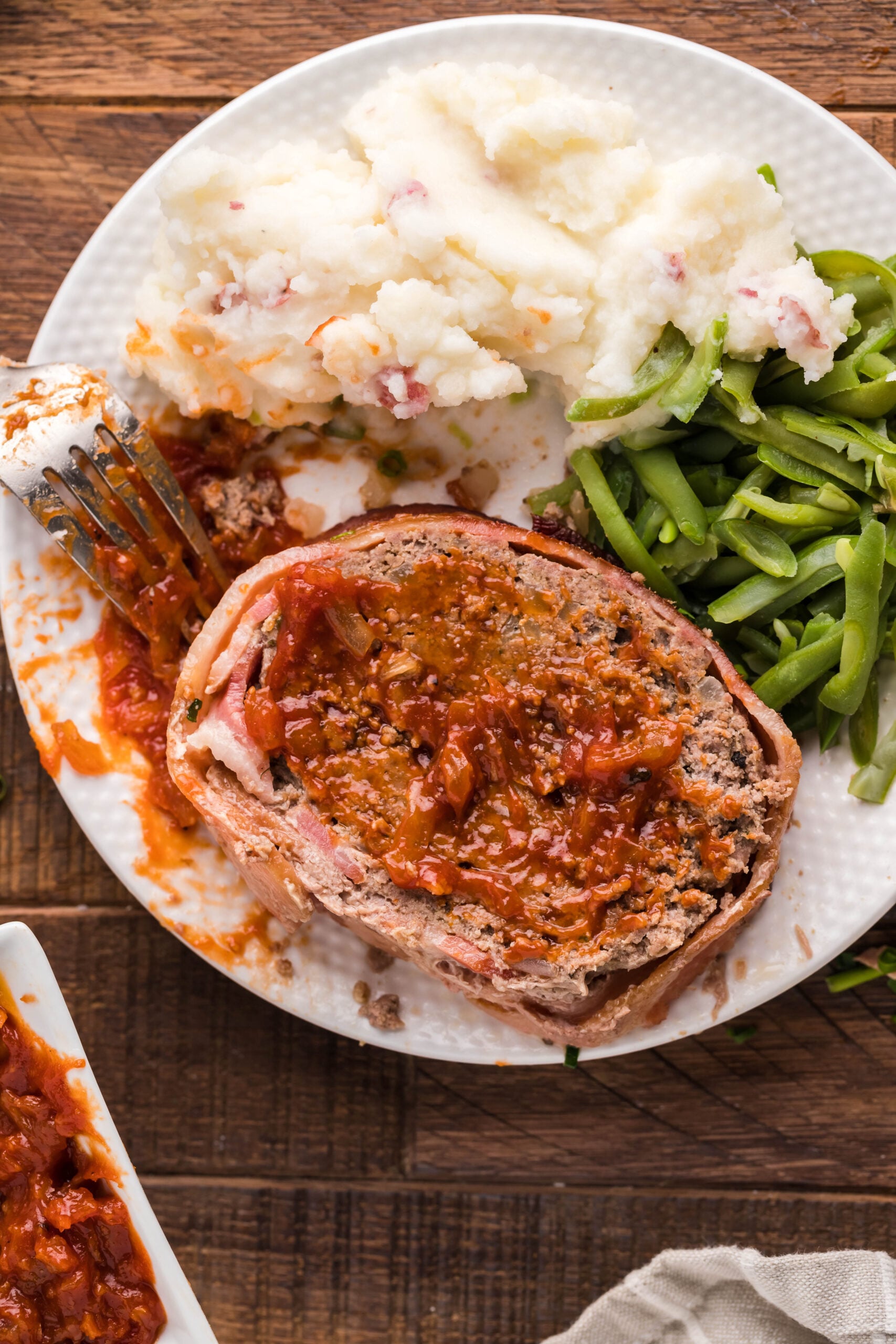 Overhead view of Bacon Wrapped Meatloaf on a white dish served with mashed potatoes and green beans.