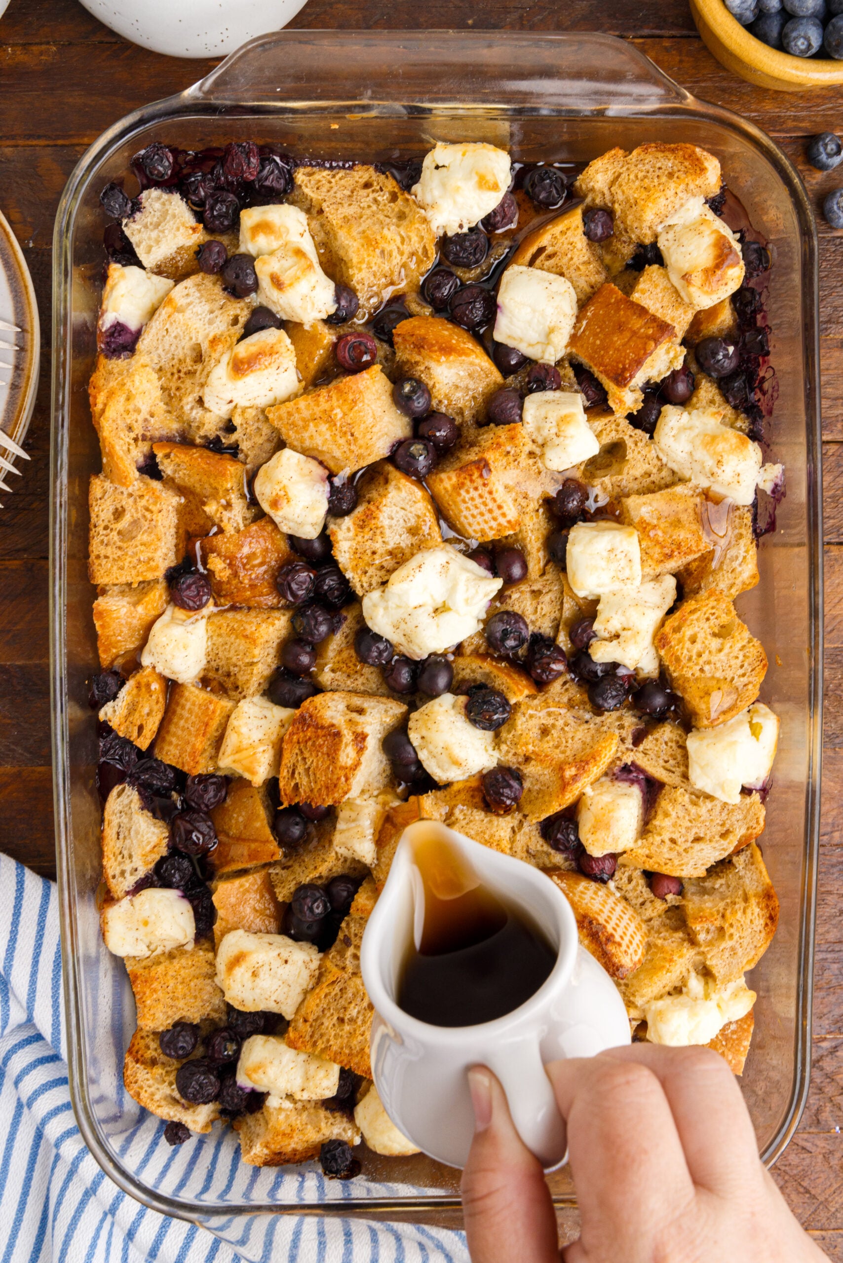 Overhead view of Blueberry French Toast Casserole in a clear baking dish with syrup being drizzled over top.