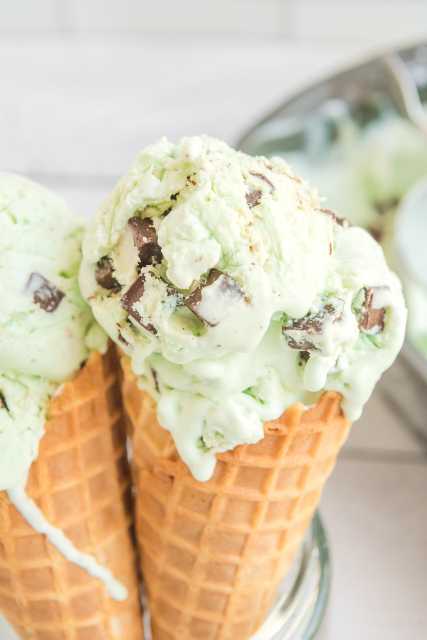 Close up view of two scoops of Mint Chocolate Chip Ice Cream in two ice cream cones.