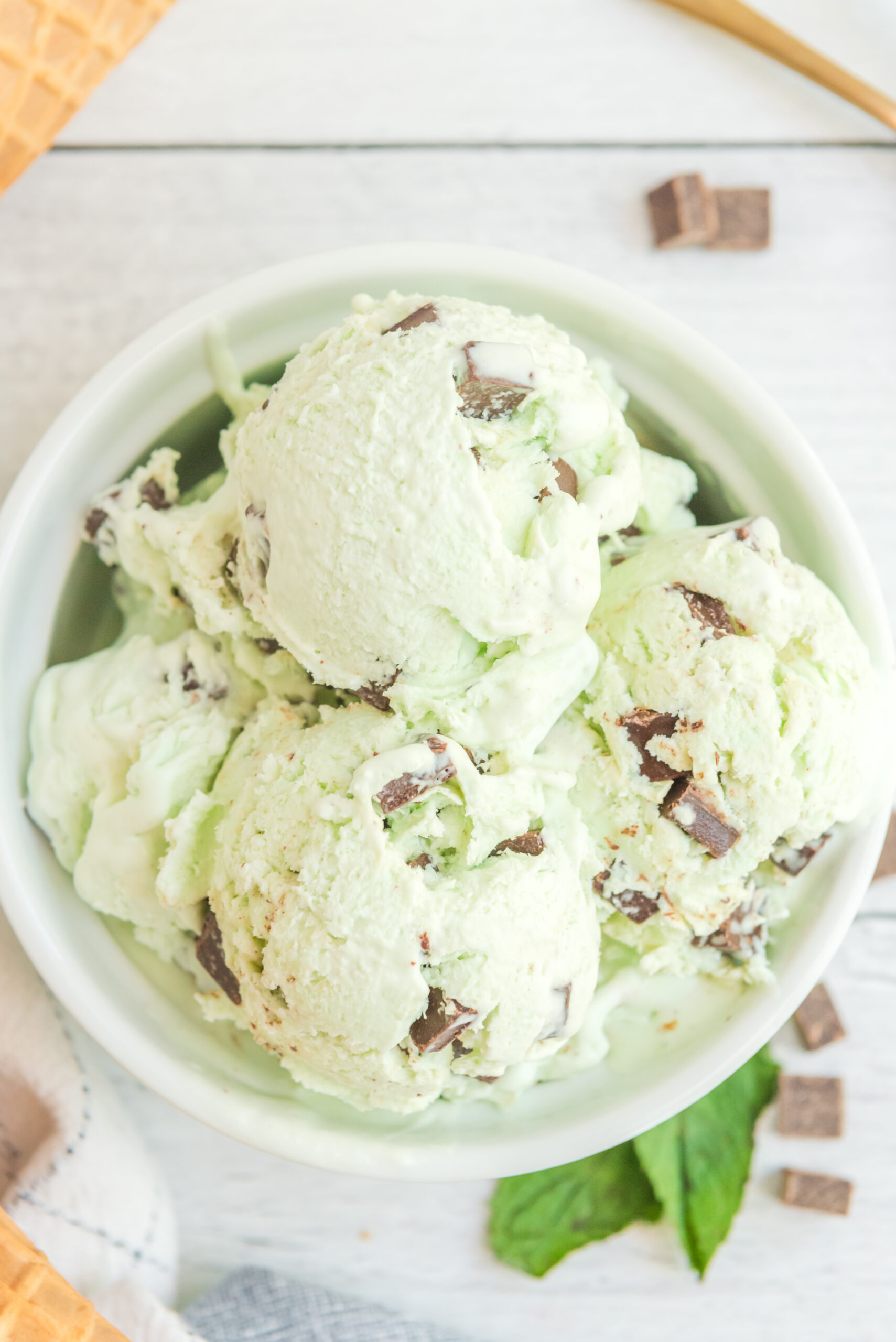 Overhead view of scoops of Mint Chocolate Chip Ice Cream in a white bowl.