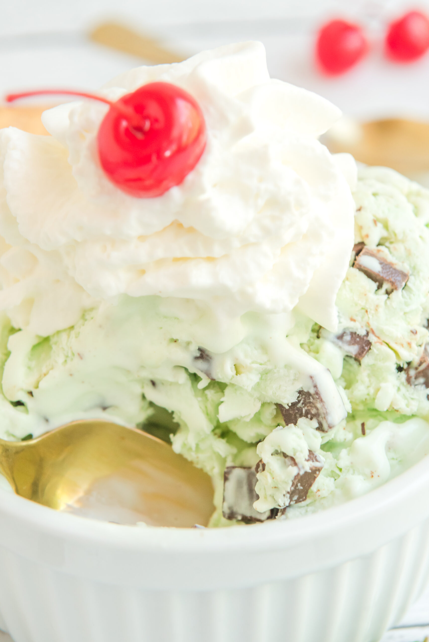 Close up view of scoops of Mint Chocolate Chip Ice Cream in a white bowl garnished with whipped cream and cherry.
