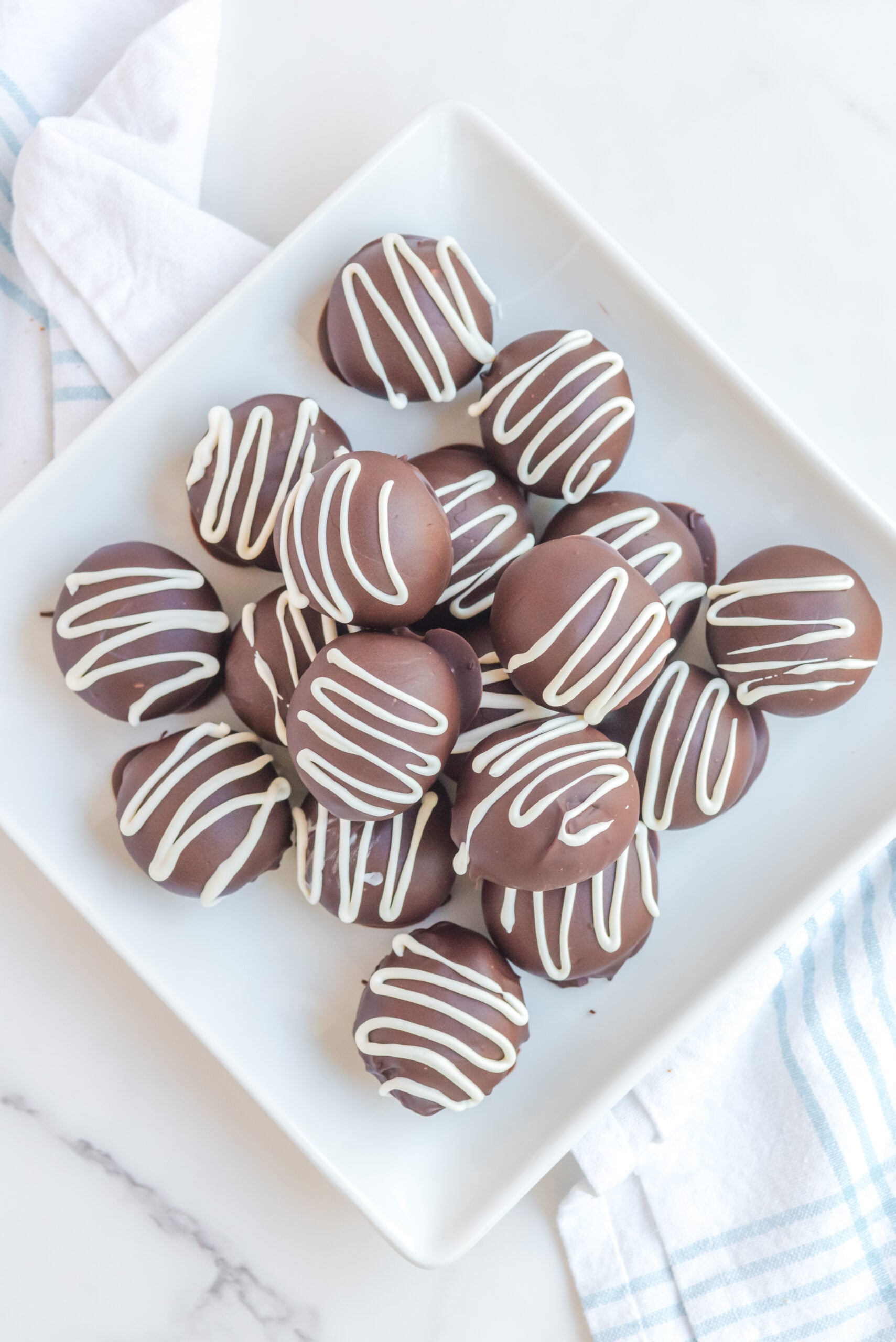 Brownie Truffles stacked on a white plate with brownies in the background.