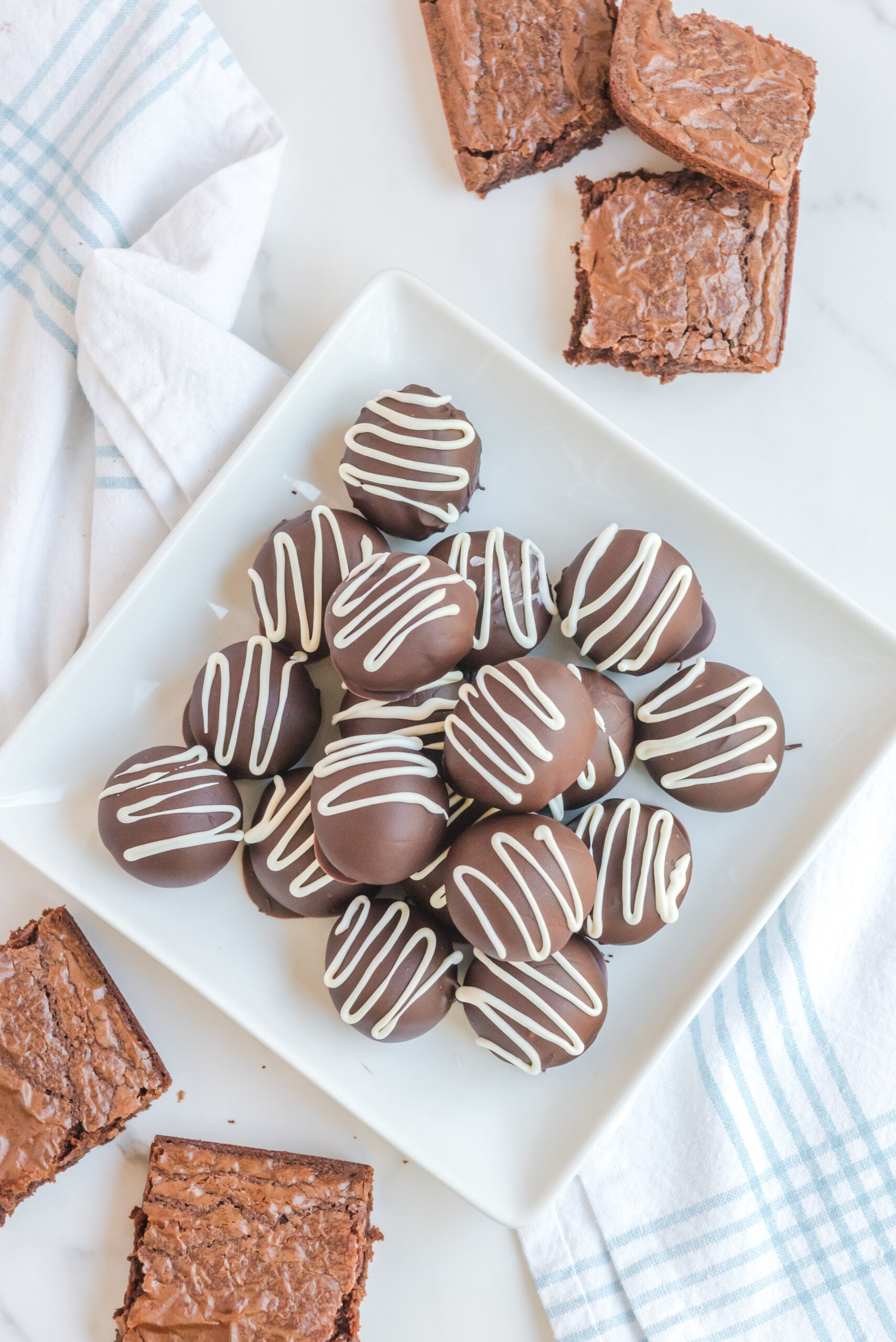Brownie Truffles stacked on a white plate with brownies in the background.