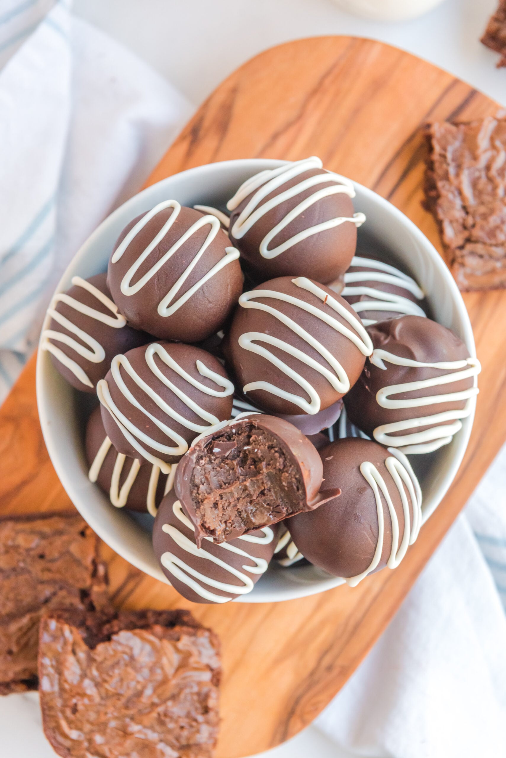 Brownie truffles stacked in a white bowl with a bite removed from the top truffle.