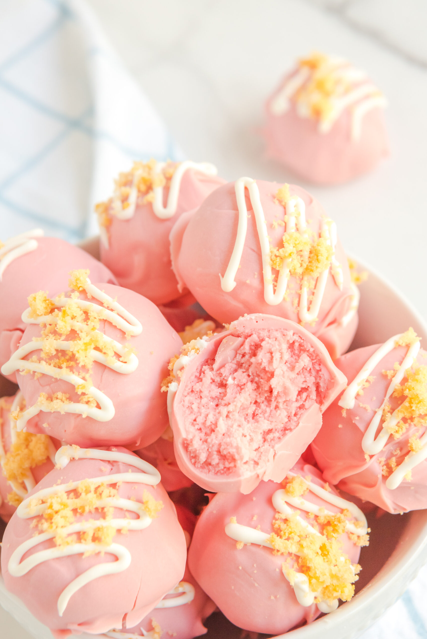 Strawberry truffles stacked on top of each other in a white bowl with a bite gone out of one