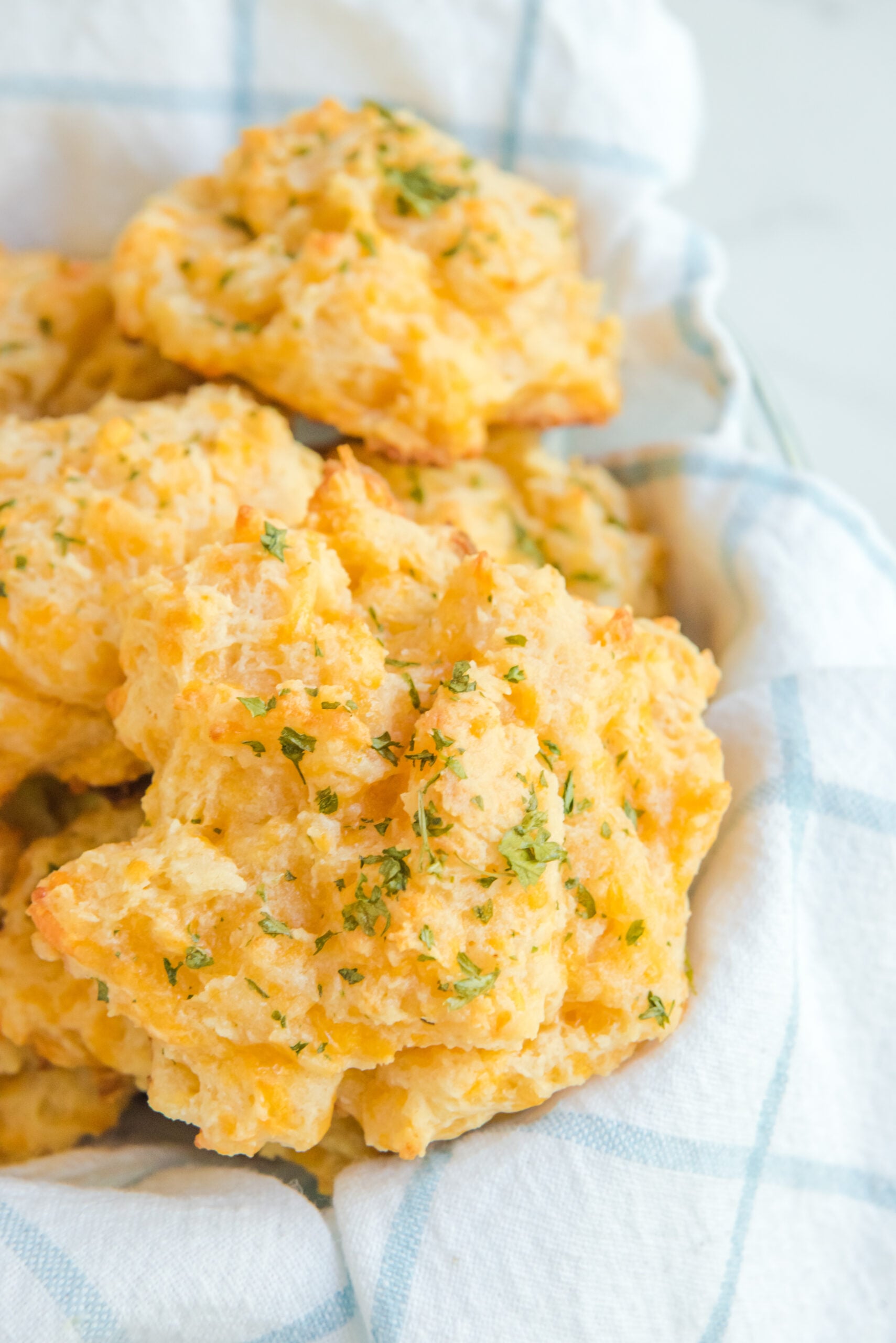 Close up shot of Copycat Red Lobster Cheddar Bay Biscuits stacked in a bowl on top of a dish towel.