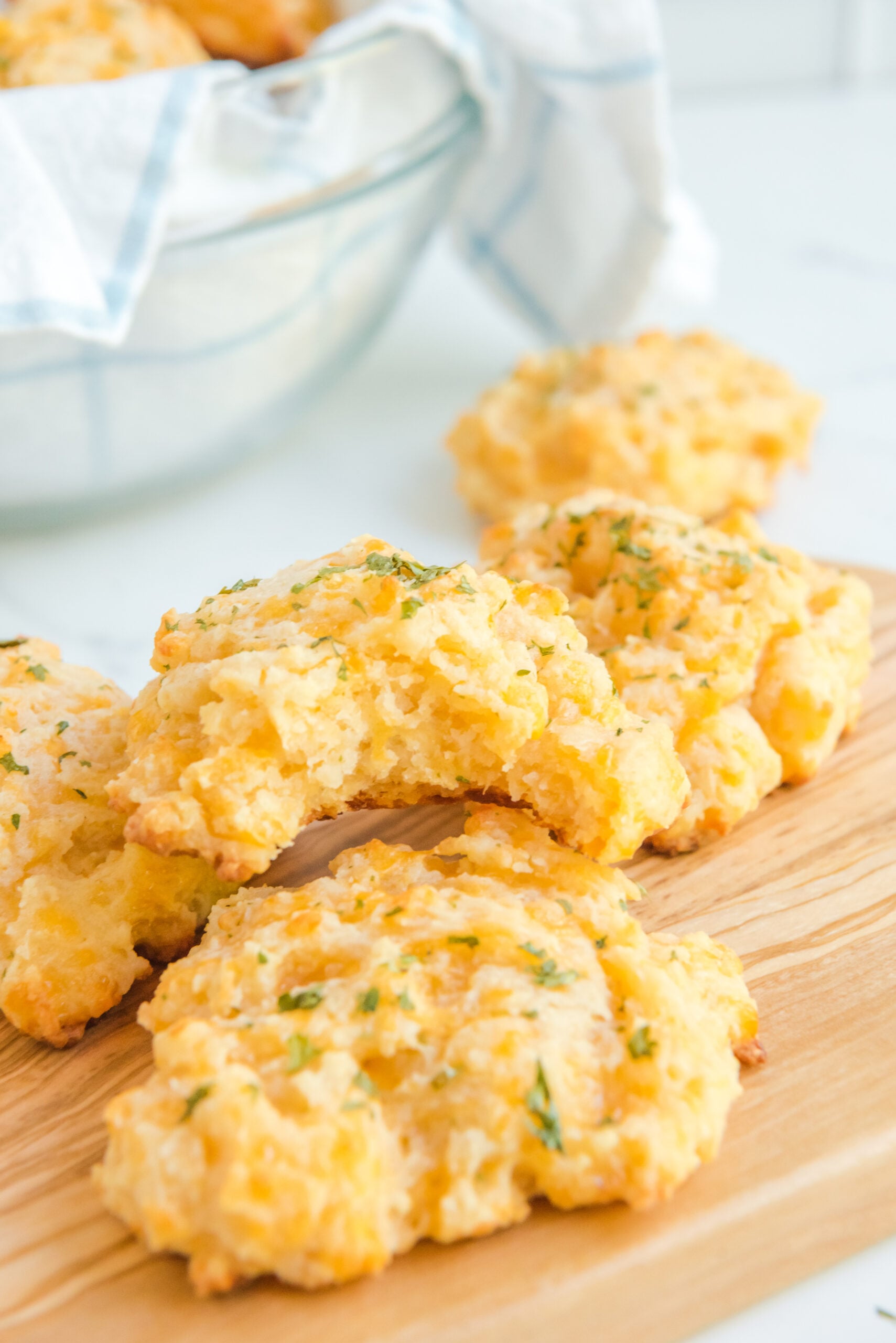 Side view of Copycat Red Lobster Cheddar Bay Biscuits with a bite taken out of one on a wooden cutting board.
