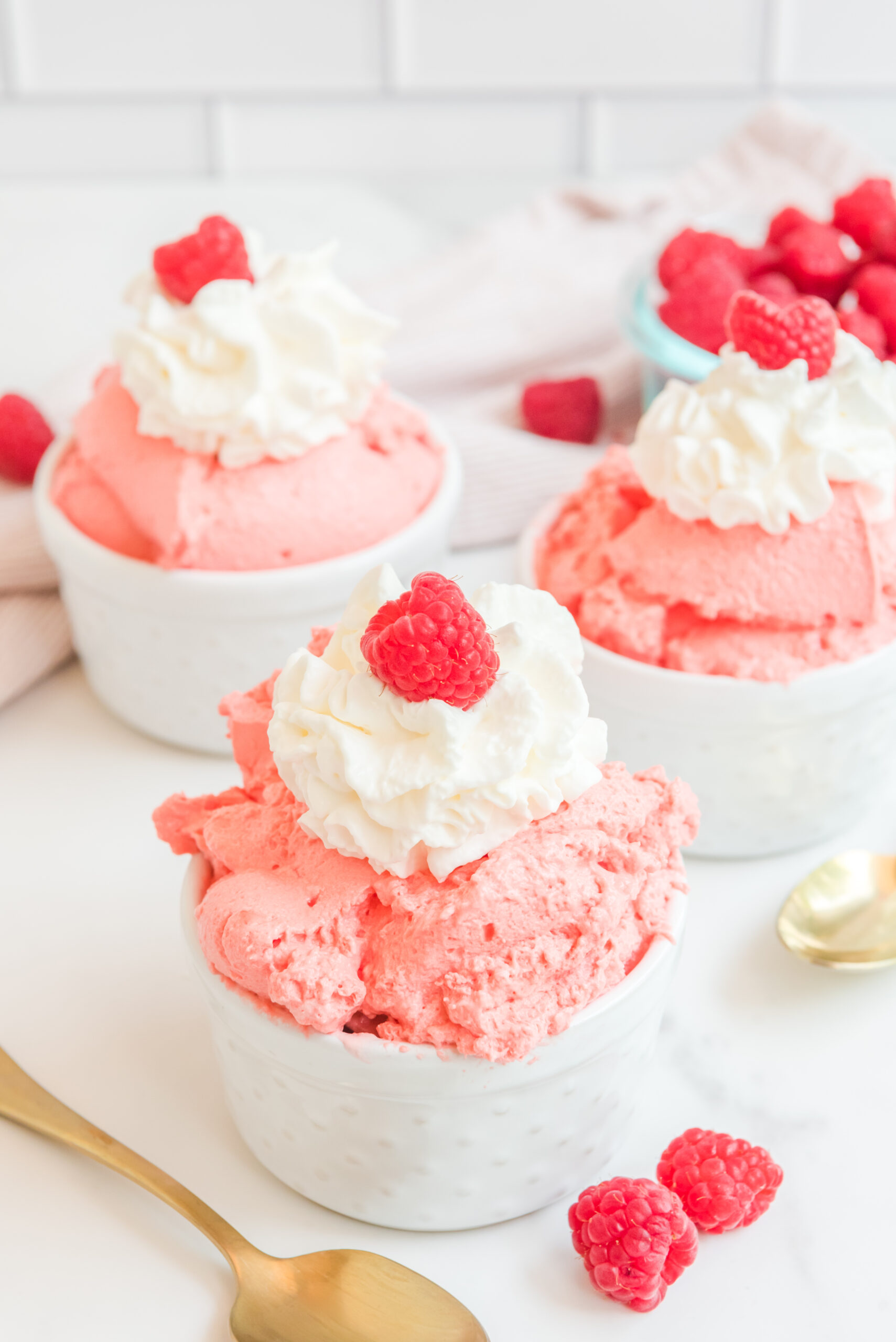 Raspberry Fluff in a white bowl topped with whipped cream and a raspberry and a gold spoon laying next to it.
