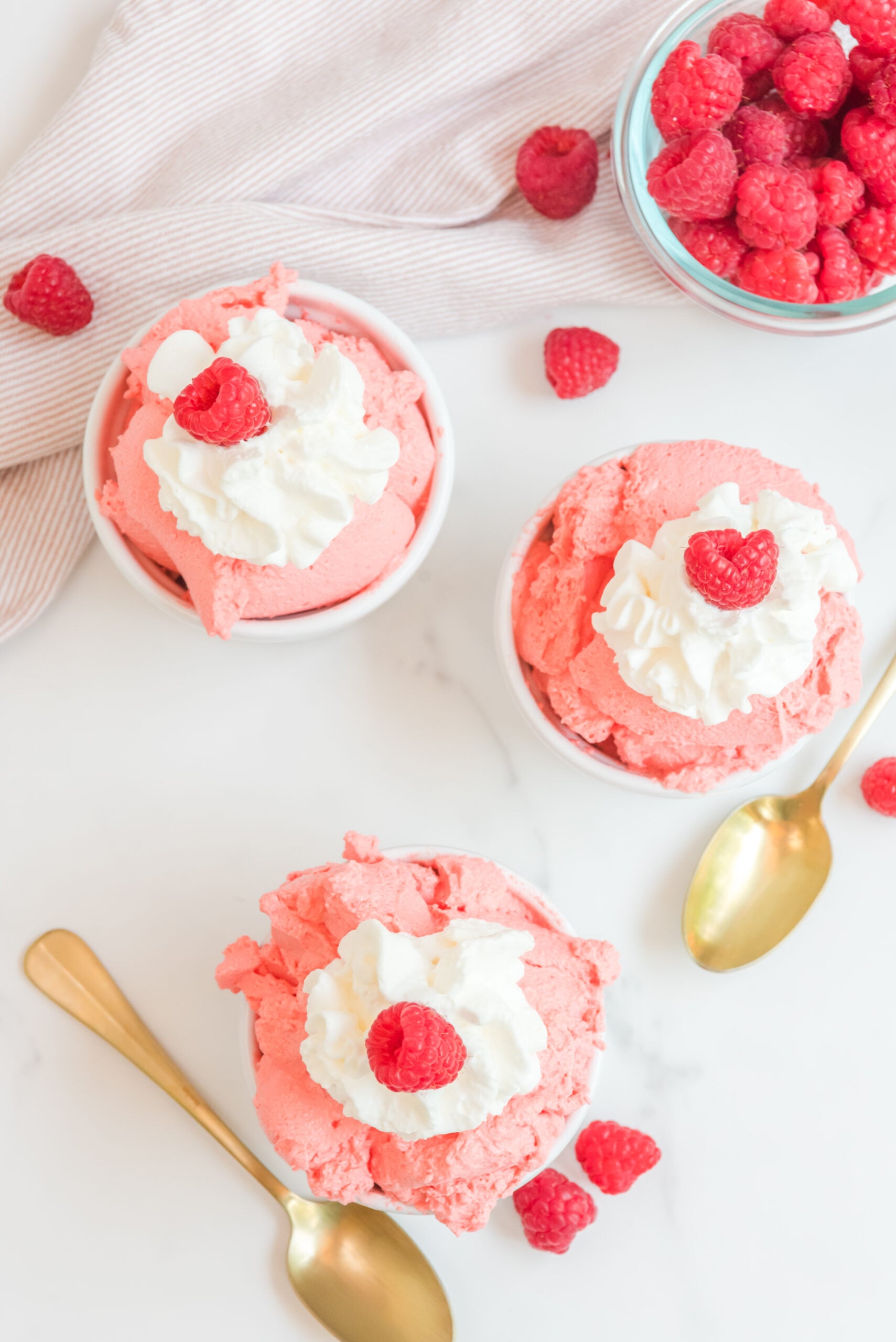Overhead view of Raspberry Jello Fluff in three white dishes garnished with whipped cream and fresh raspberries.