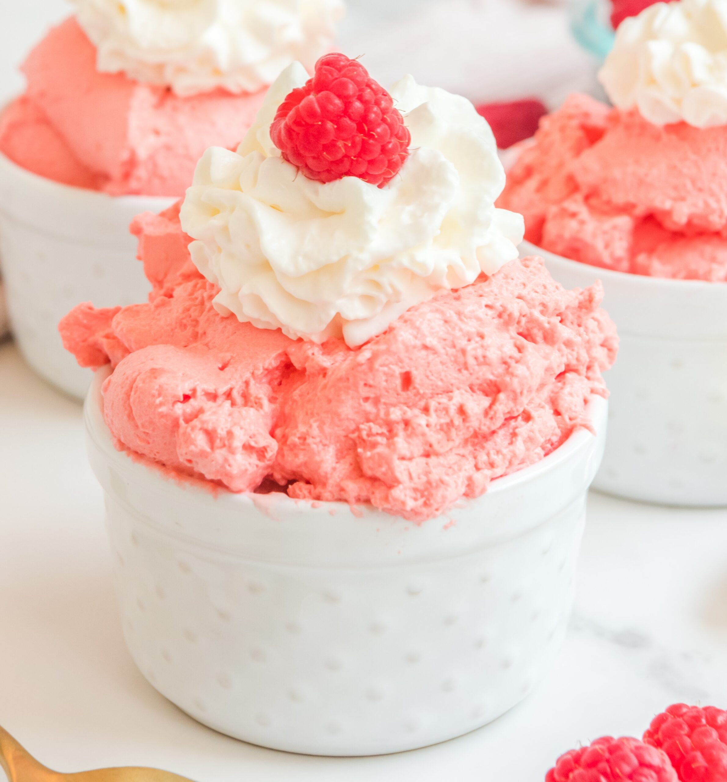 Raspberry Fluff in a white bowl topped with whipped cream and a raspberry