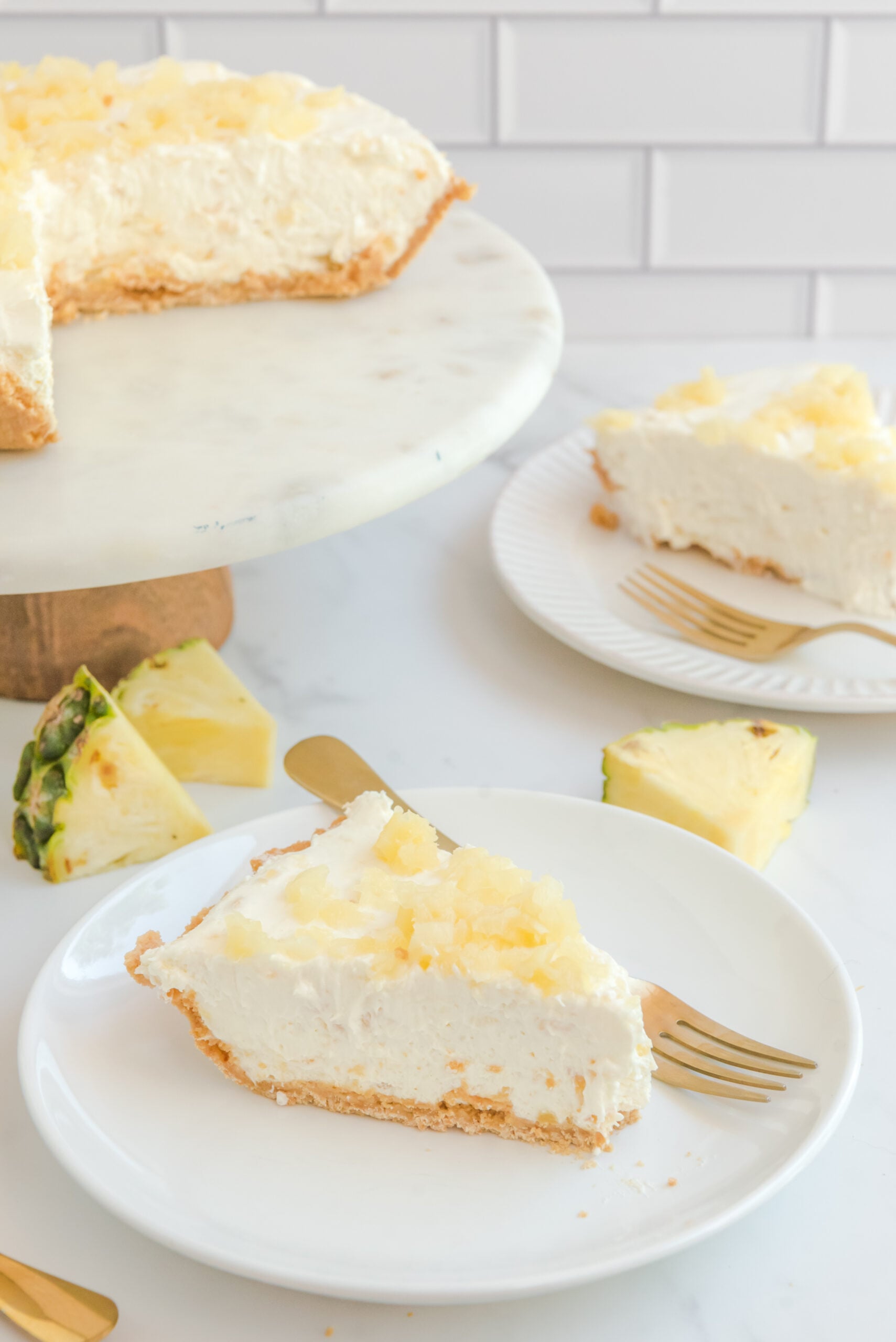 Front view of a slice of No Bake Pineapple Cheesecake on a white plate served with a gold fork.