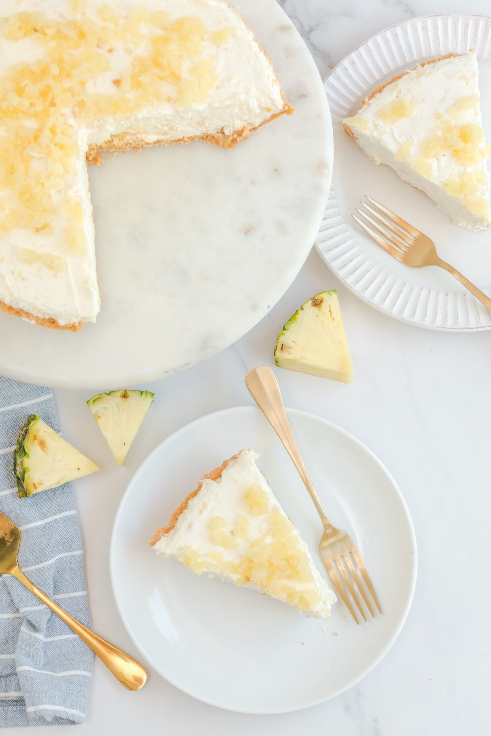 Overhead view of No Bake Pineapple Cheesecake with two slices removed and served on a white plate with gold forks.