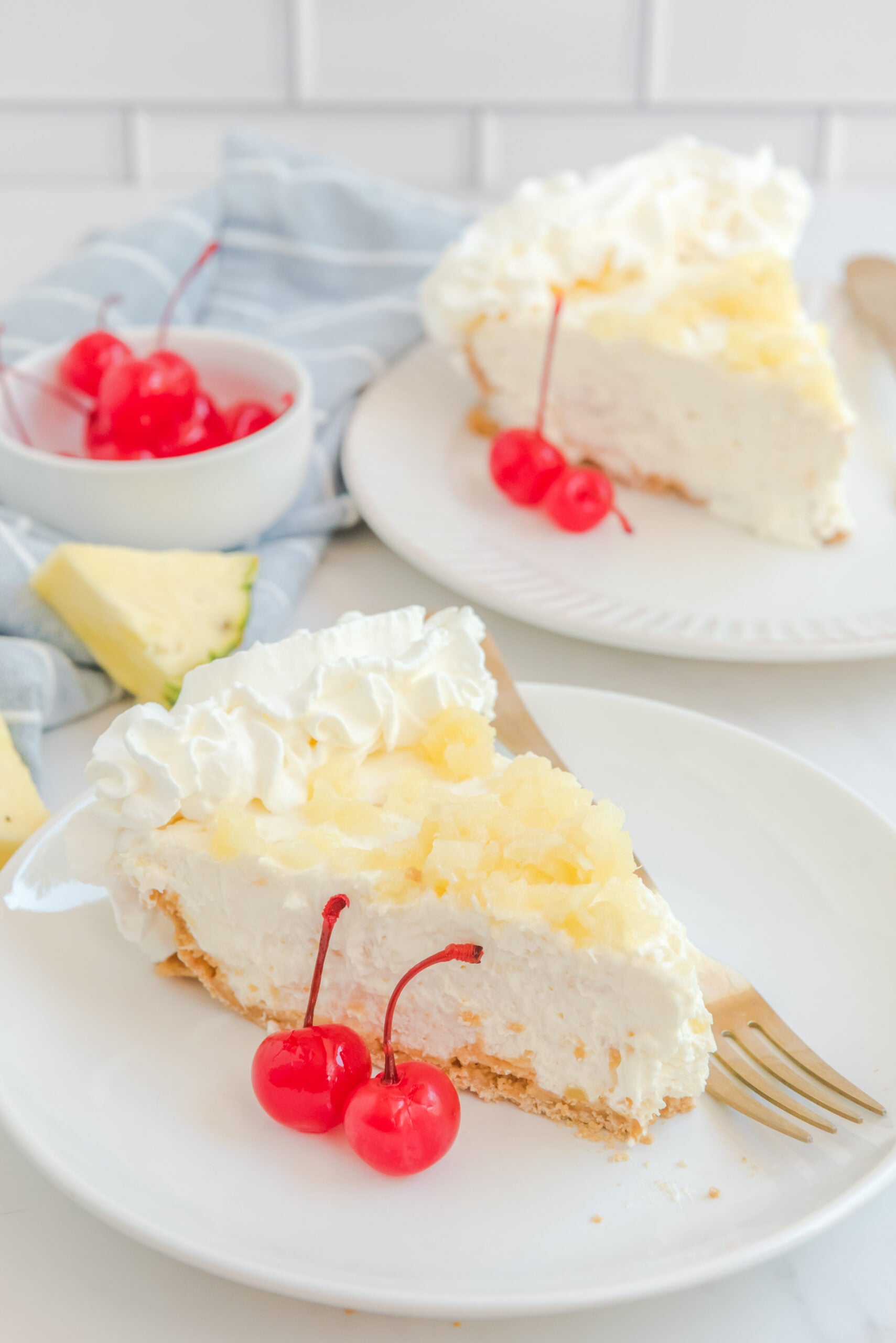 No Bake Pineapple Cheesecake Pie on a white plate with maraschino cherries next to a slice 