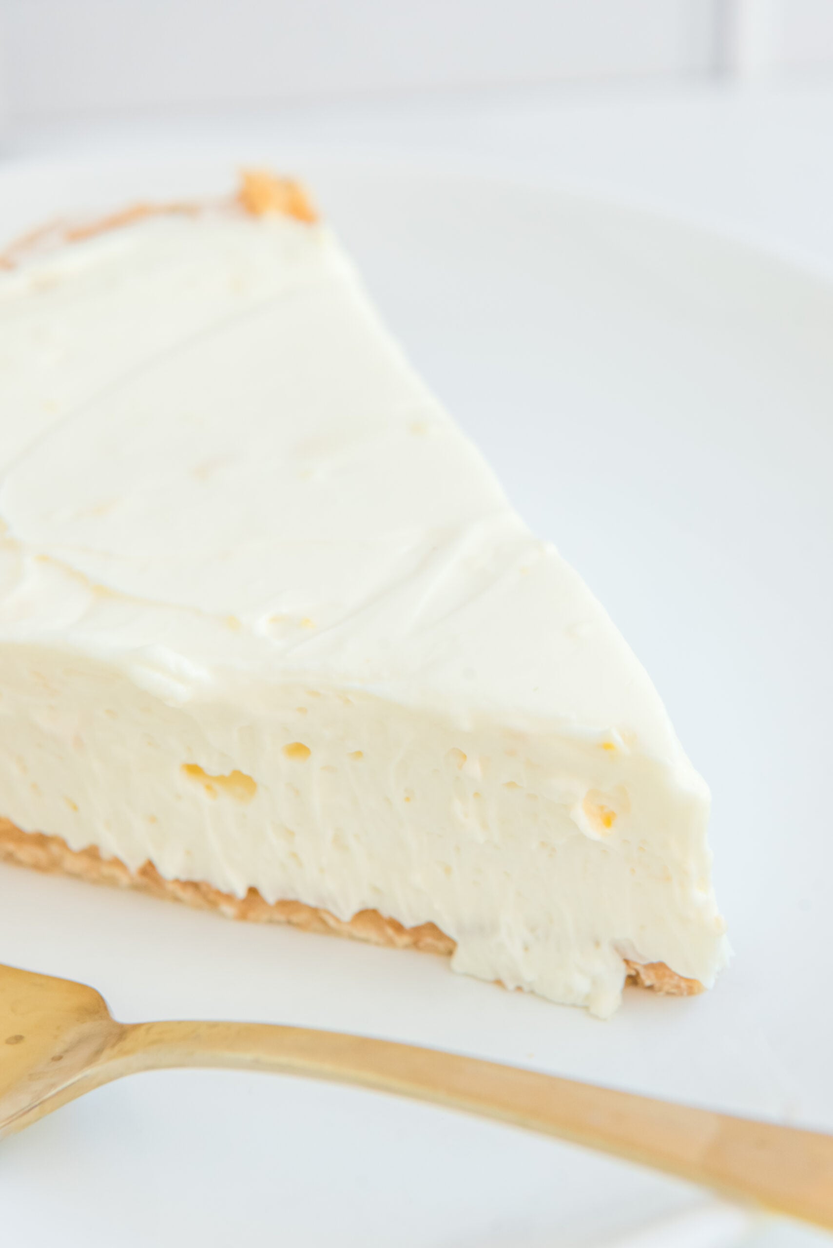 Close up view of a slice of No Bake Lemon Cheesecake on a white plate served with a gold fork.