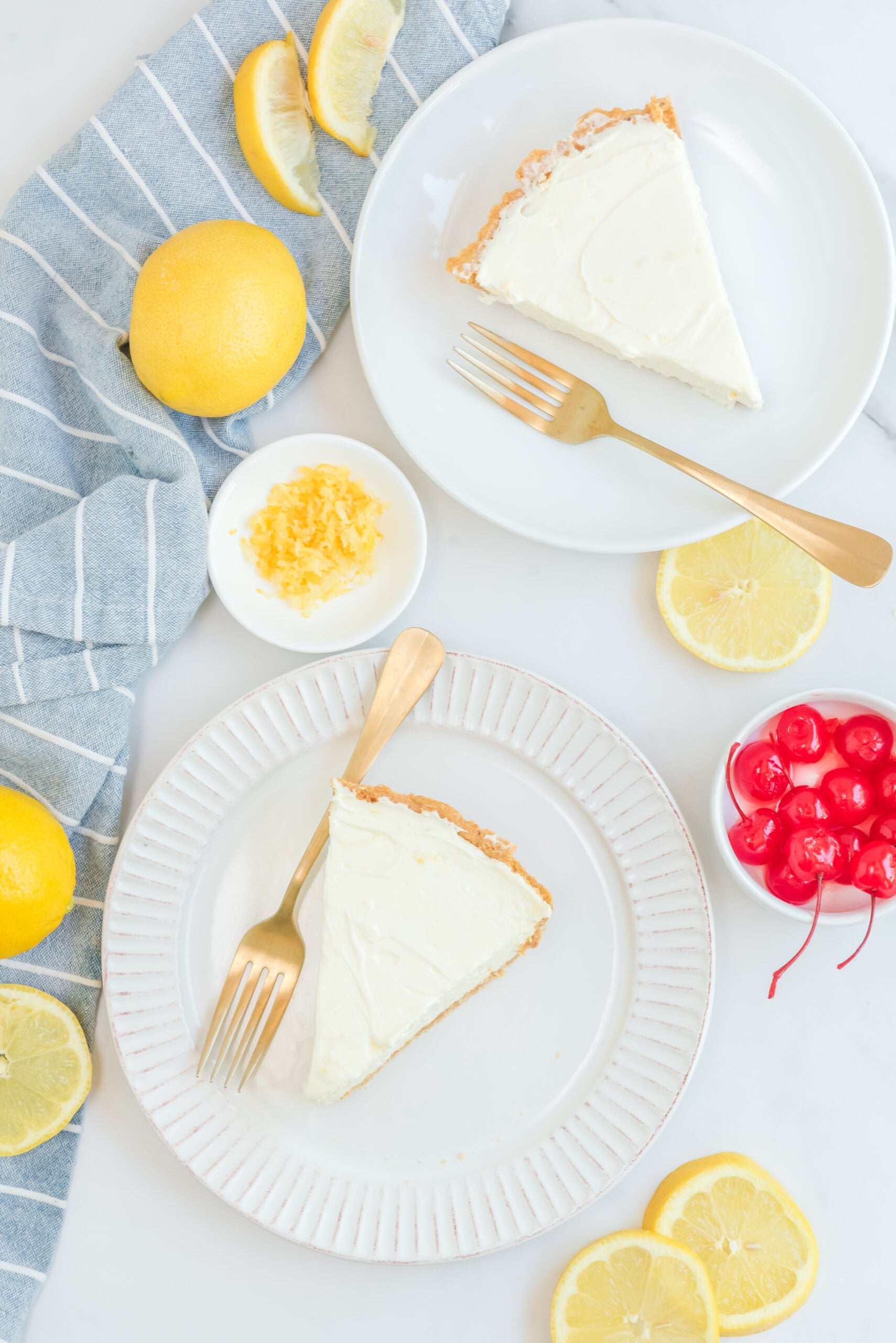 Overhead view of two slices of No Bake Lemon Cheesecake on white plates served with gold forks.