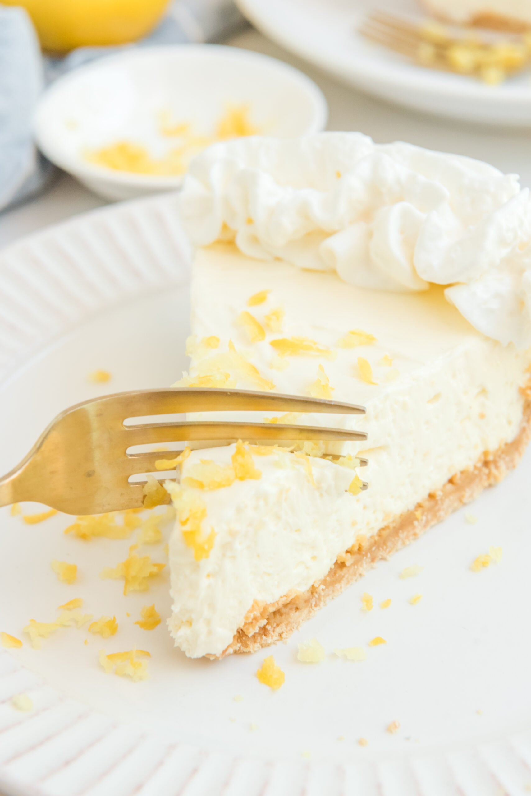 Close up view of a gold fork removing a bite from a slice of No Bake Lemon Cheesecake.