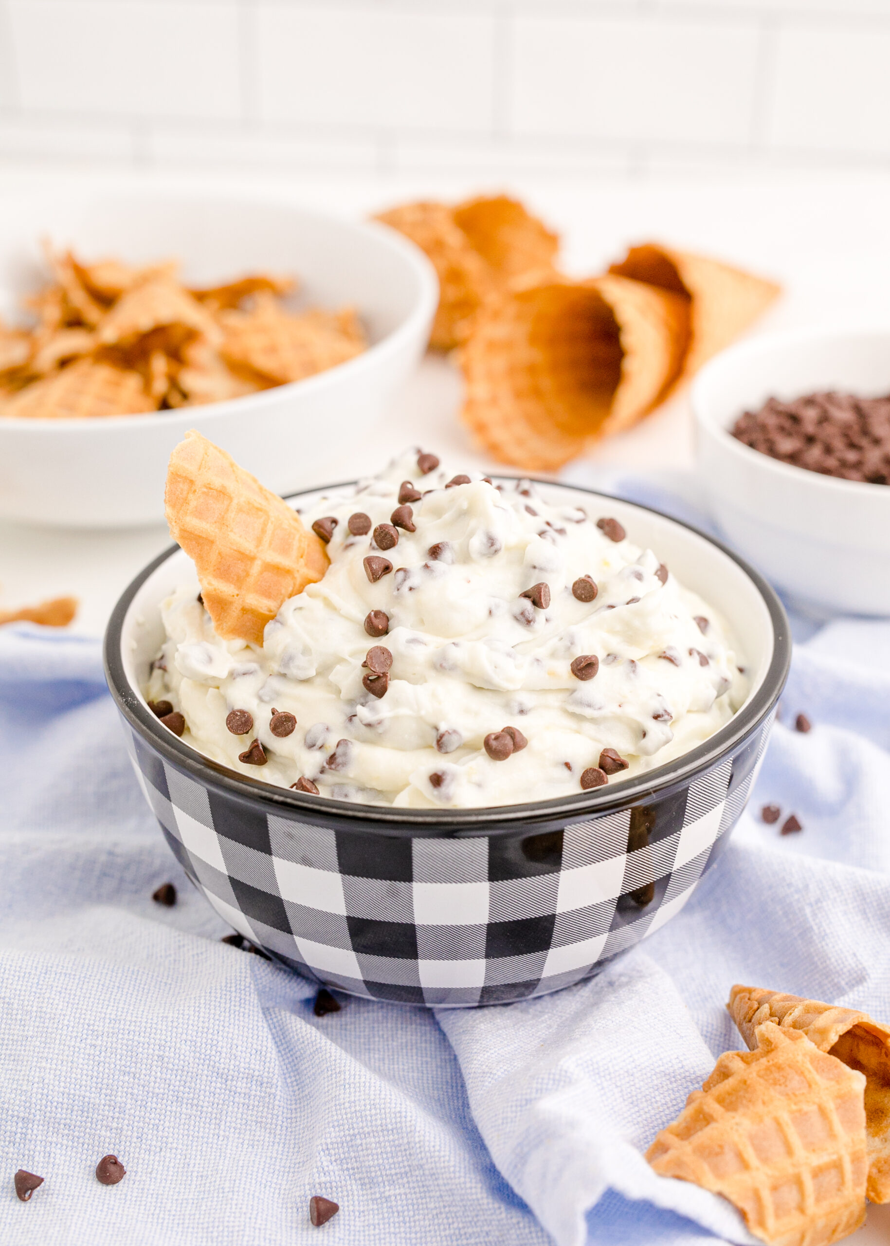 Side view of Cannoli Dip in a black and white dish with a piece of waffle cone.