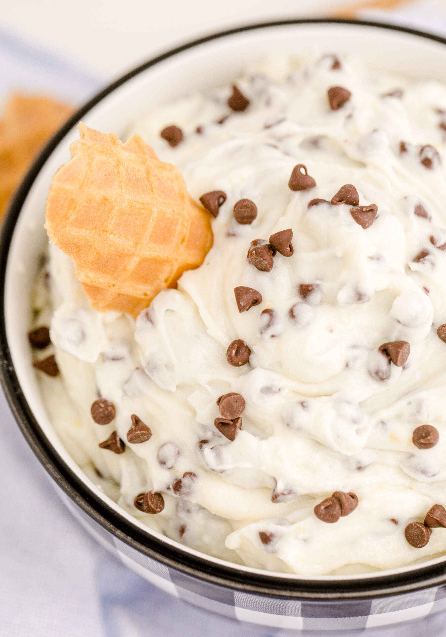 Up close overhead view of Cannoli Dip in a black and white dish with a piece of waffle cone.