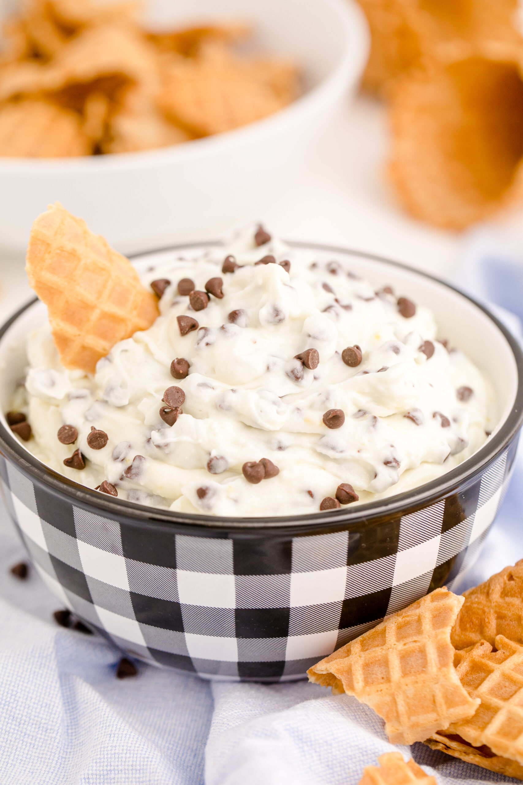 Side view of Cannoli Dip in a black and white dish with a piece of waffle cone.