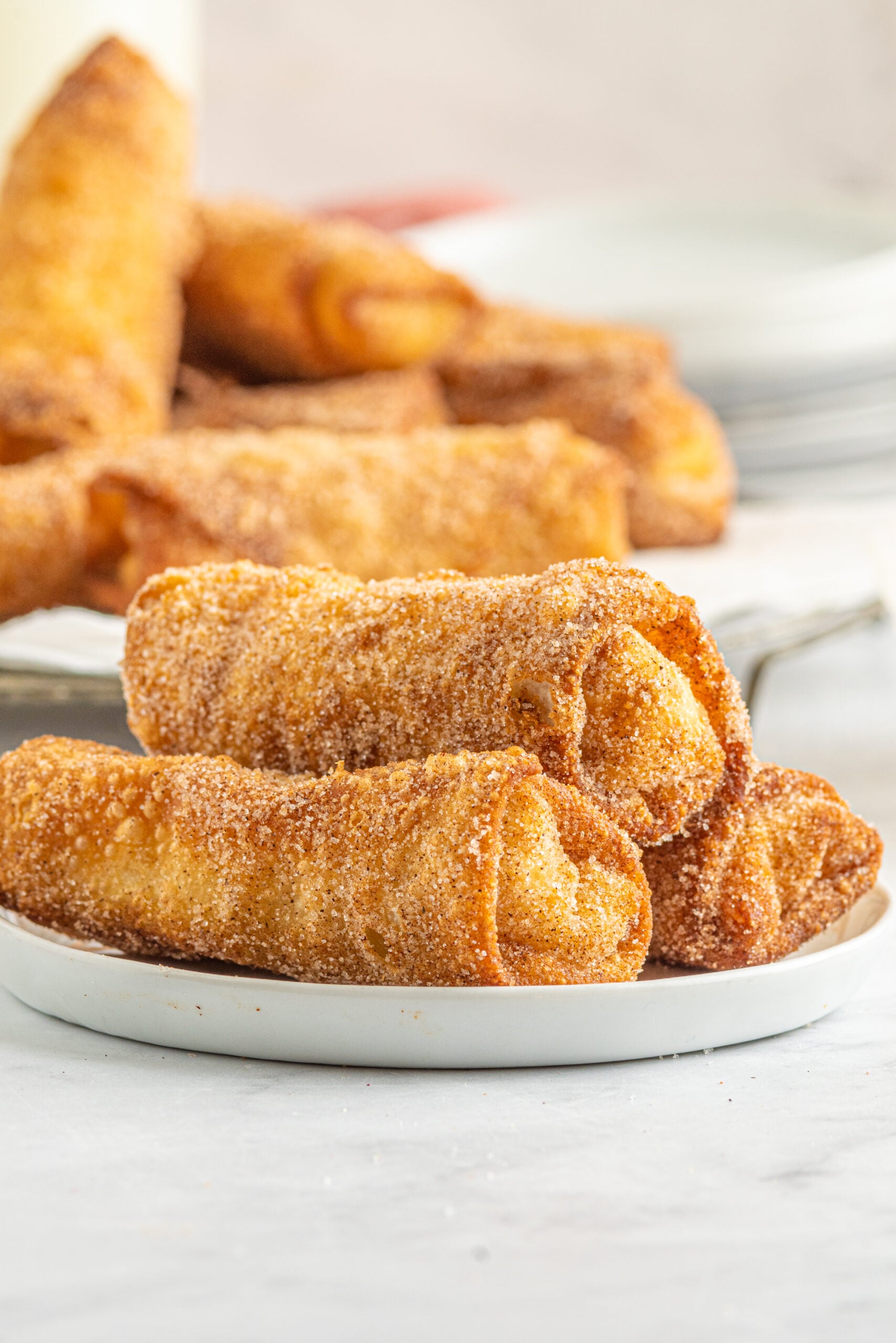 Front view of three Cheesecake Egg Rolls stacked on a white plate.