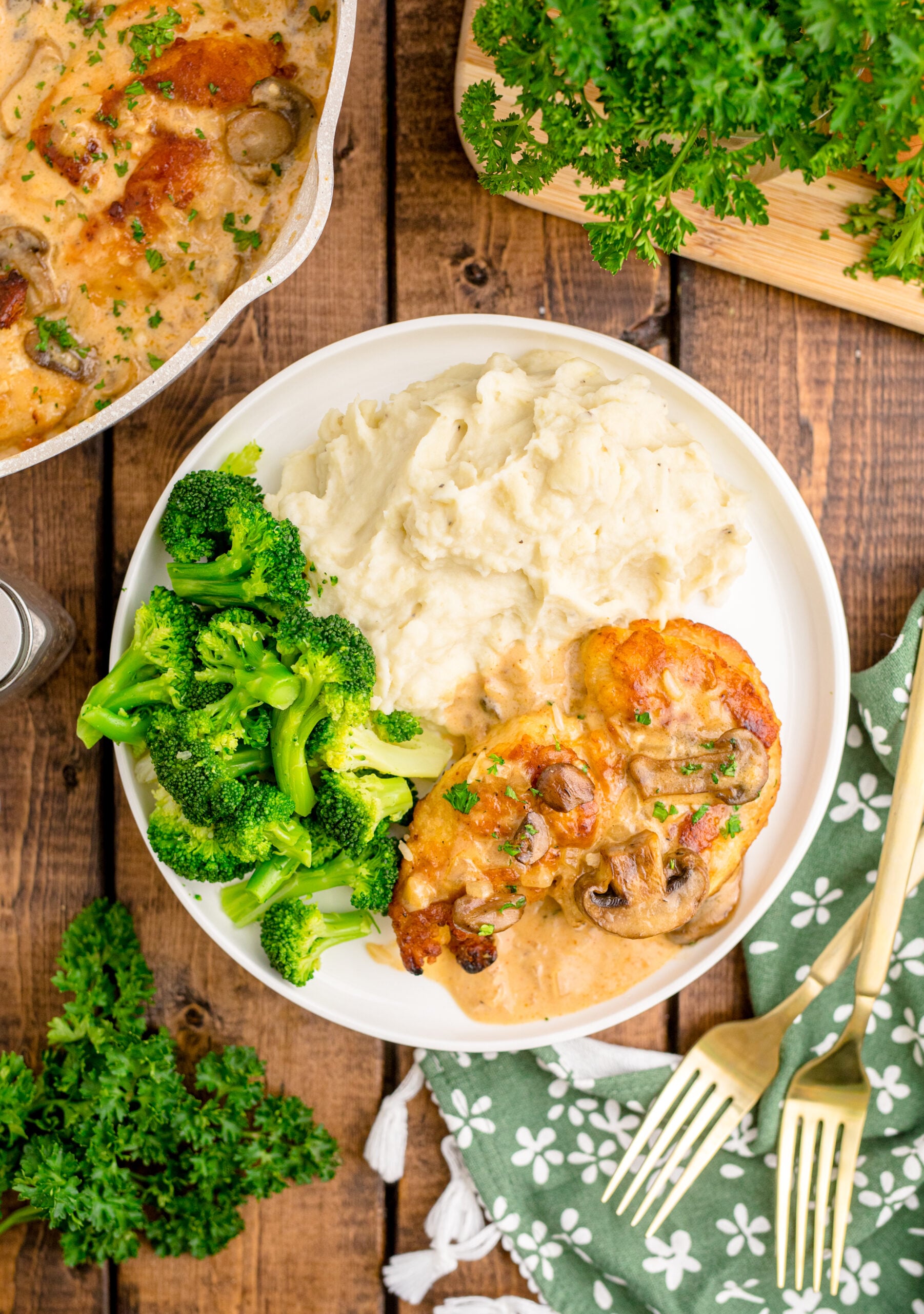 Overhead view of Chicken Marsala on a white dish served with mashed potatoes and broccoli.