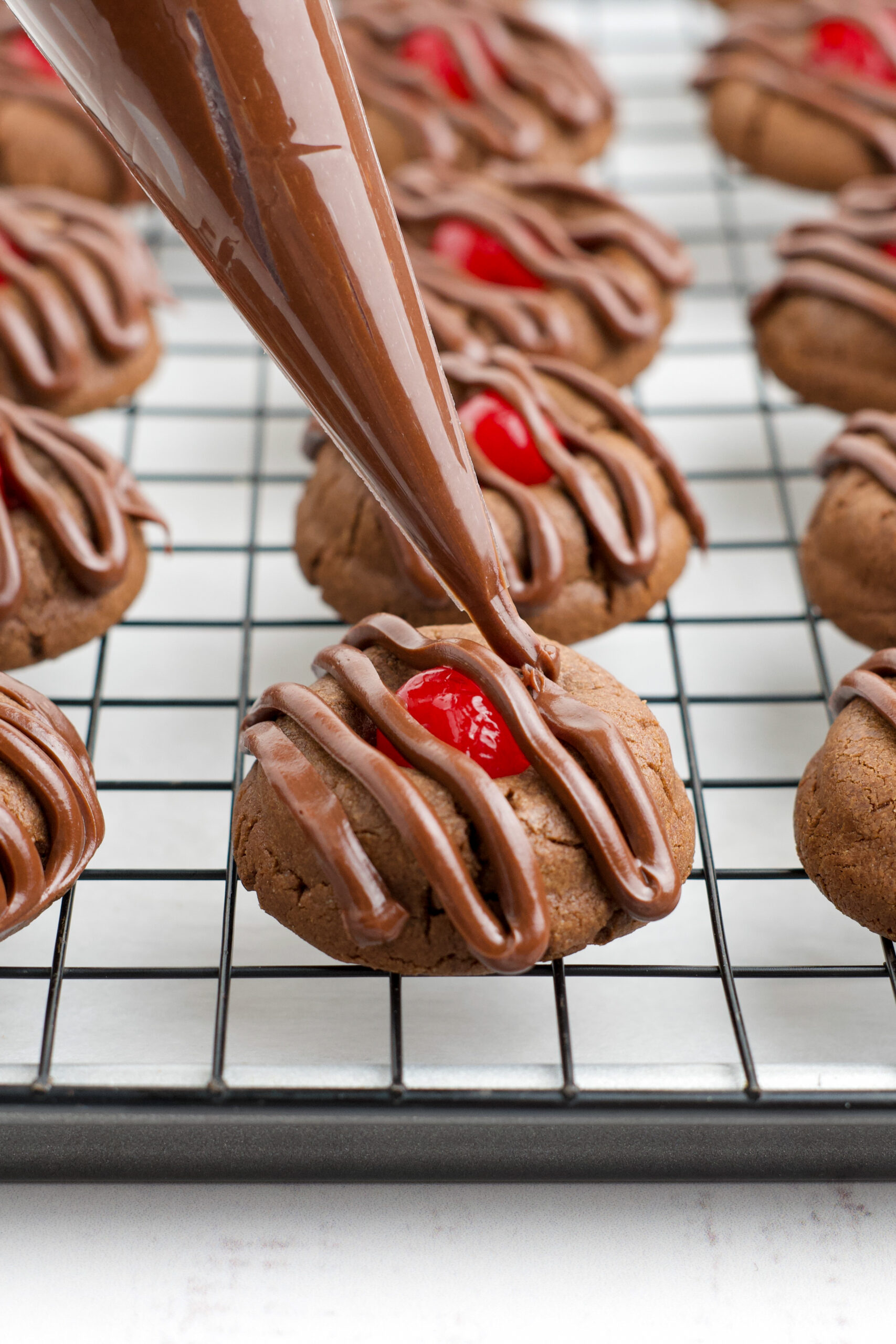 A piping bag piping on the chocolate cherry frosting onto a cookie. 