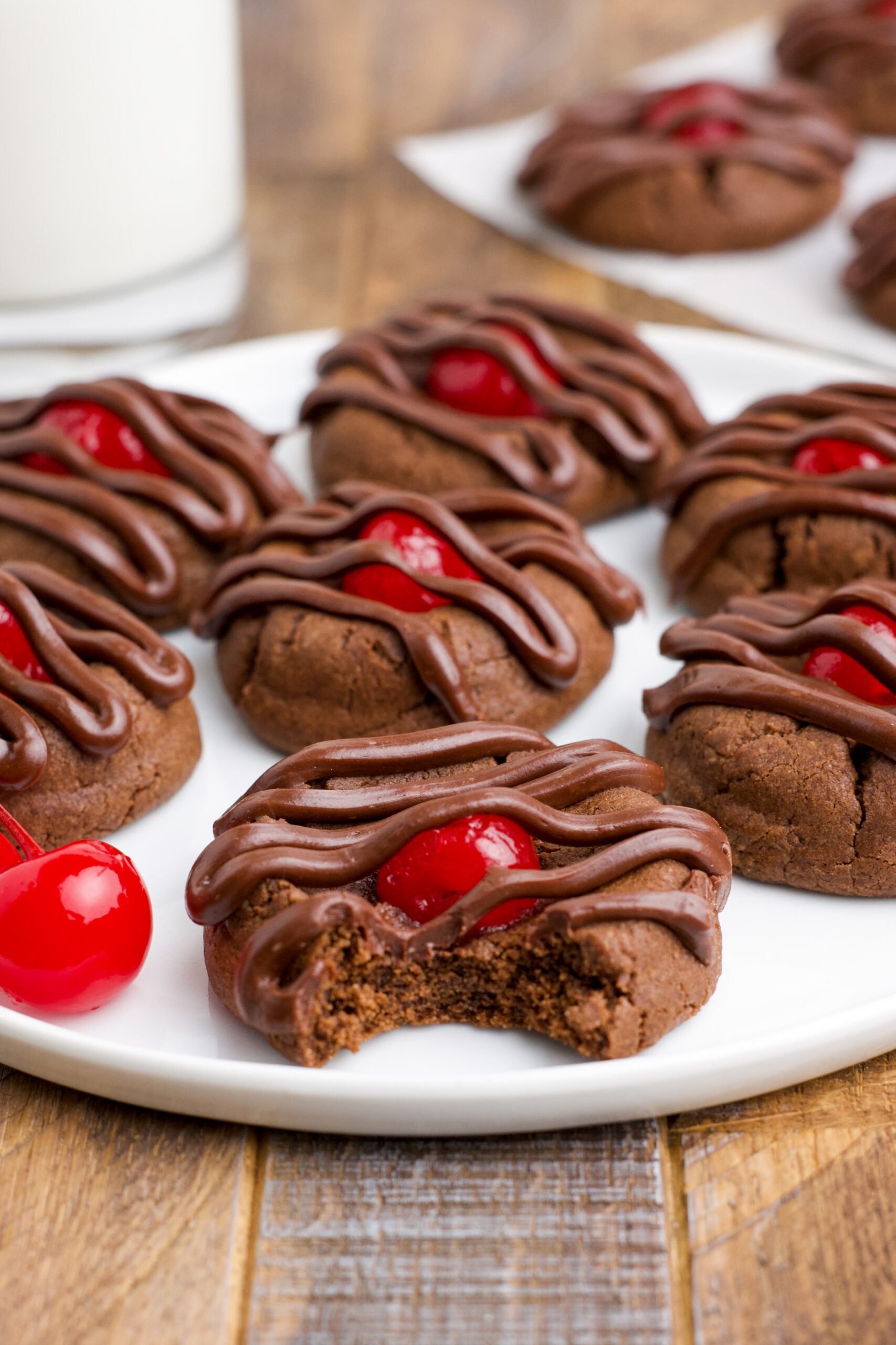 Chocolate Cherry Cookies on a white plate with a bite removed from the front cookie showing the texture inside. 