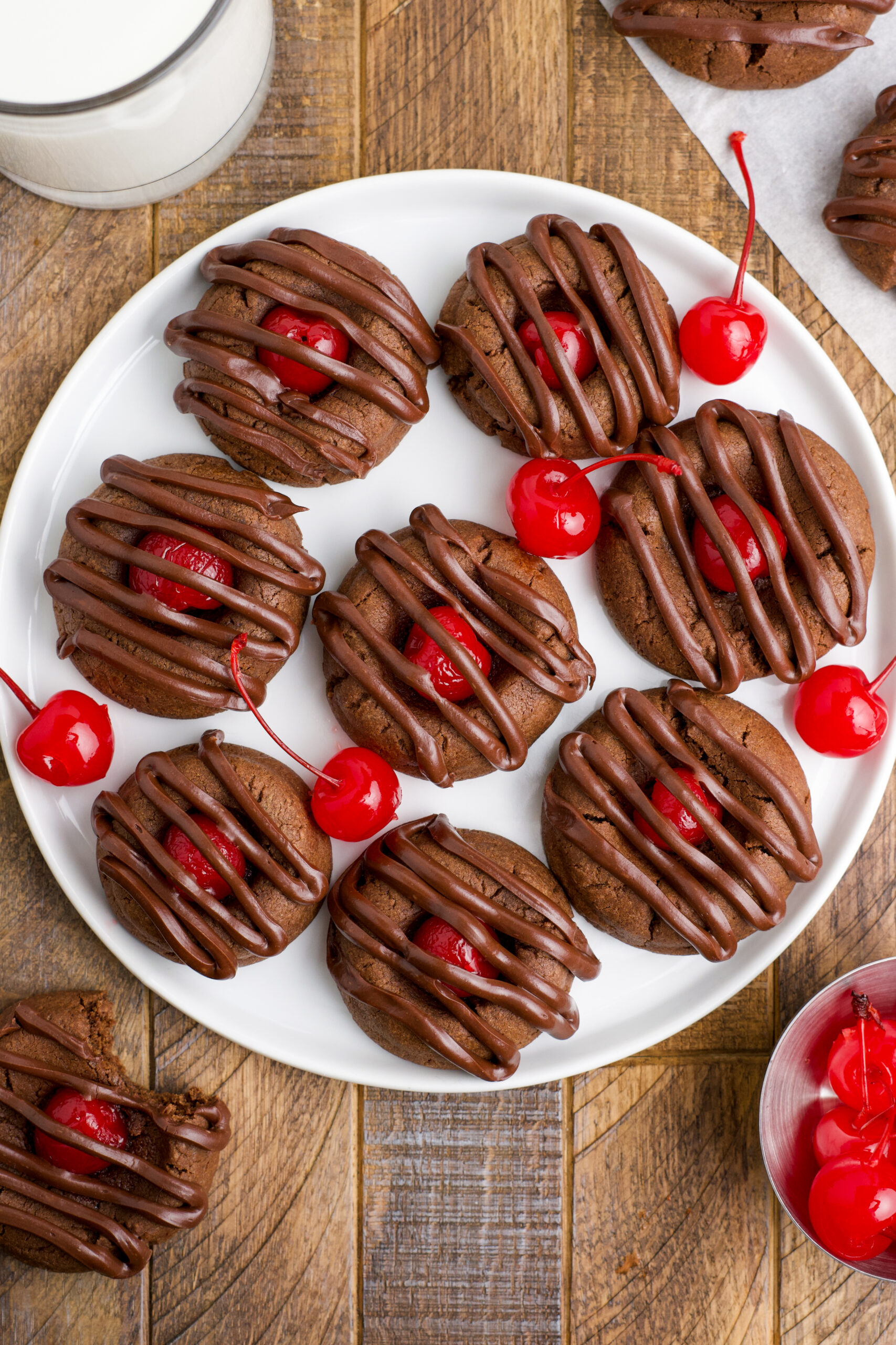 Overhead view of Chocolate Cherry Cookies on a white plate with maraschino cherries in the background. 