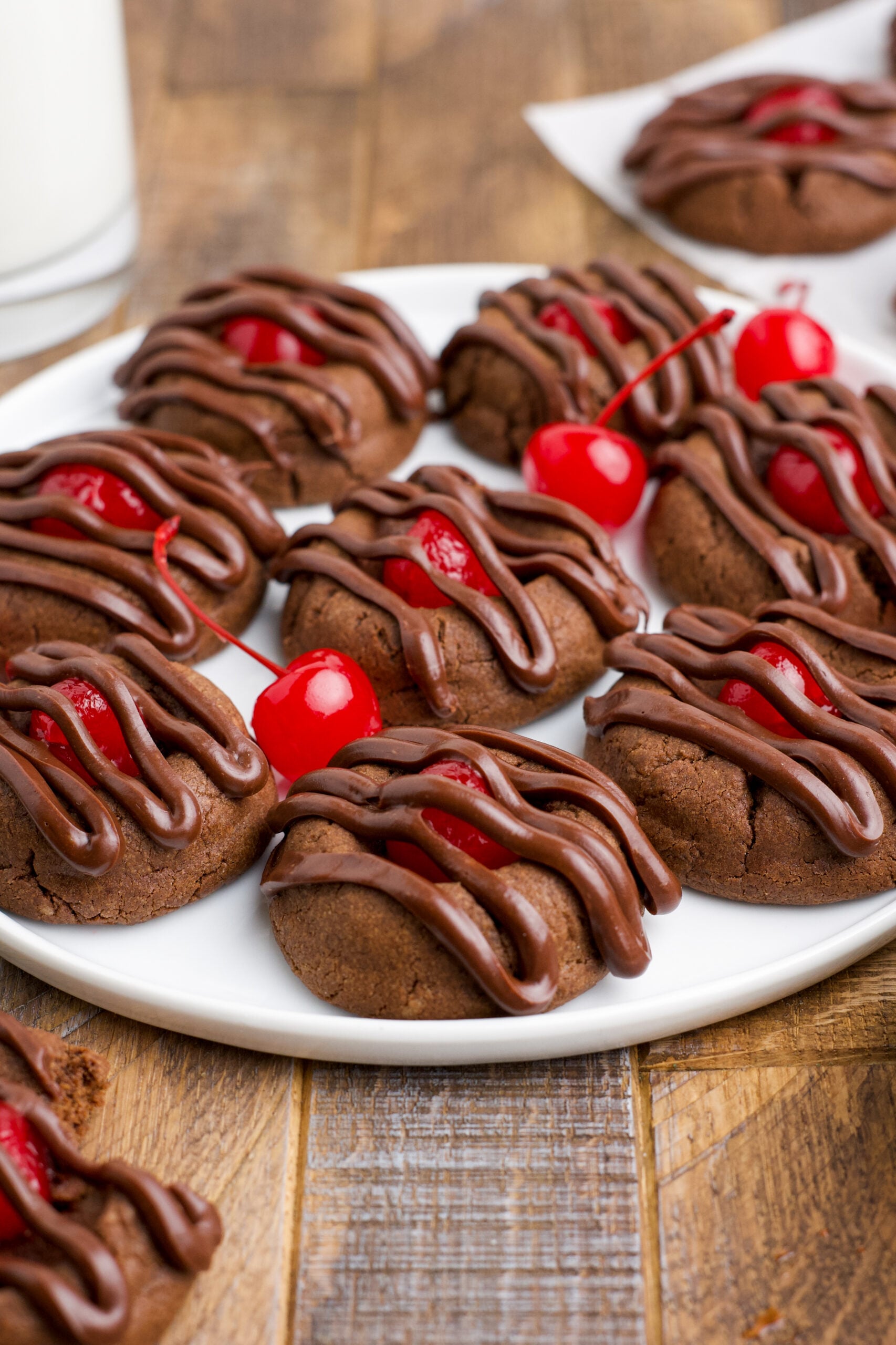 Chocolate Cherry Cookies on a white plate with maraschino cherries in the background. 