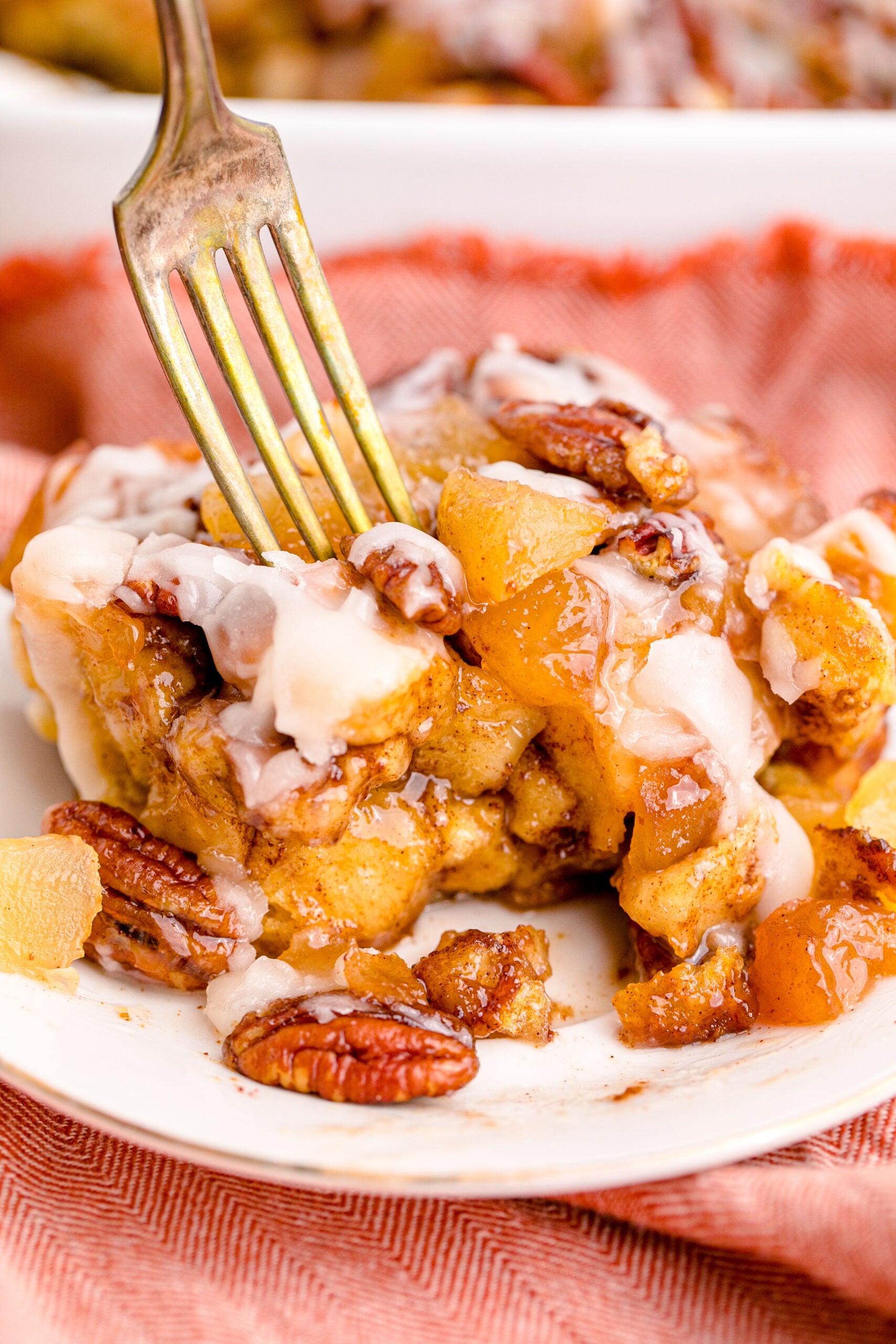 Cinnamon Roll Casserole on a white plate with a gold fork removing a bite.