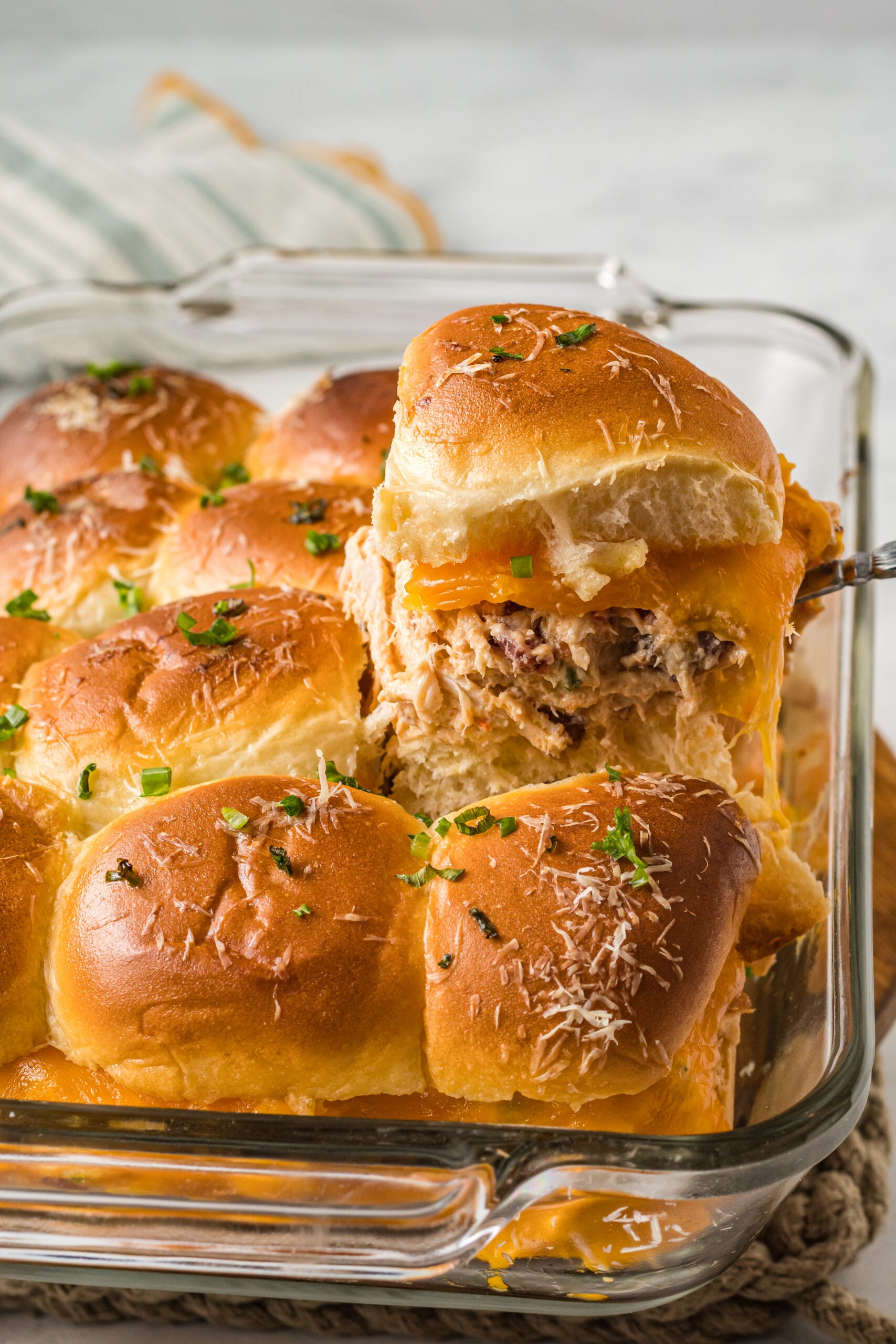 Side view of Crack Chicken Sliders in a clear baking dish with one being lifted by a silver utensil.