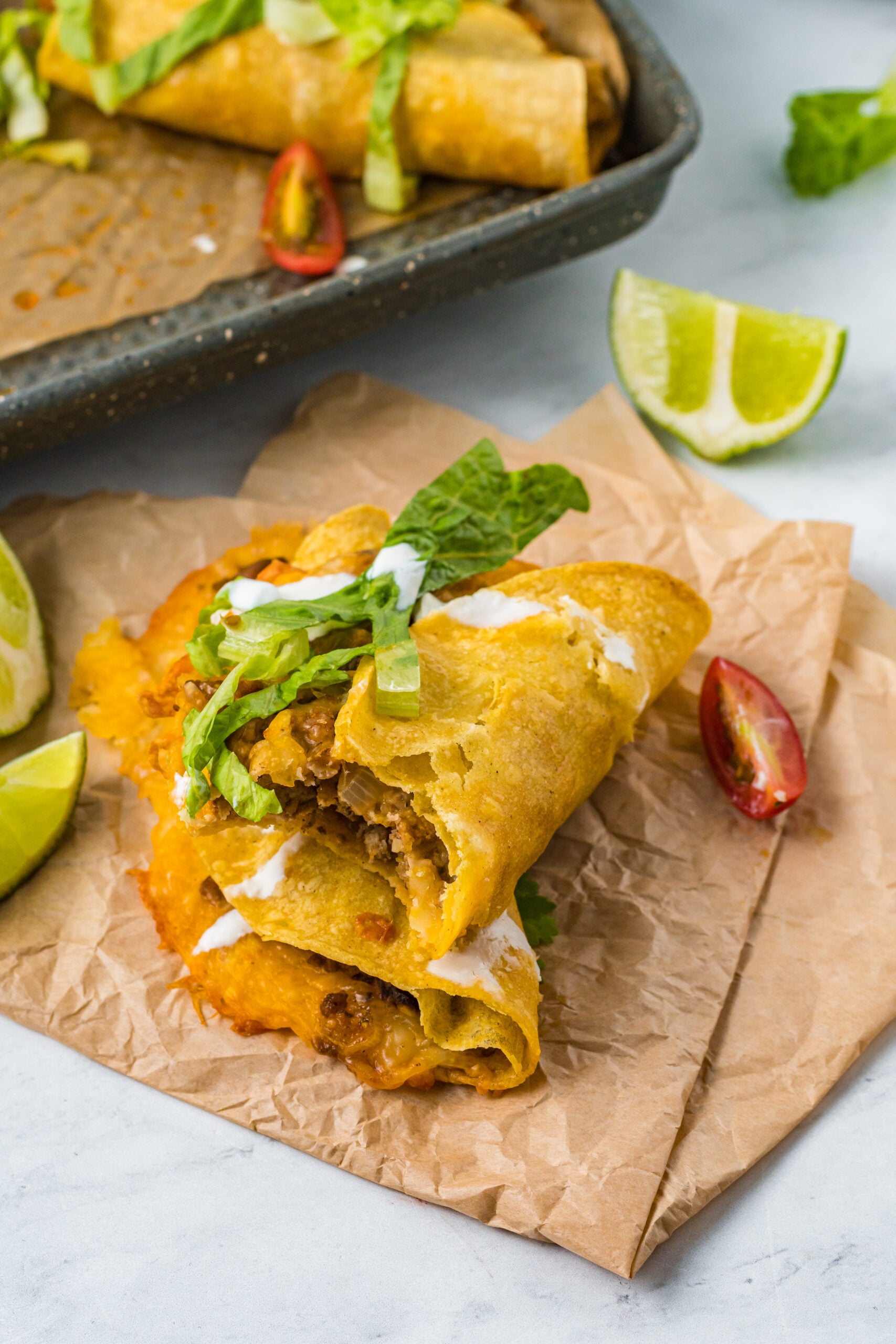 Front view of two Beef Tacos stacked on parchment paper with a bite removed from the top taco.