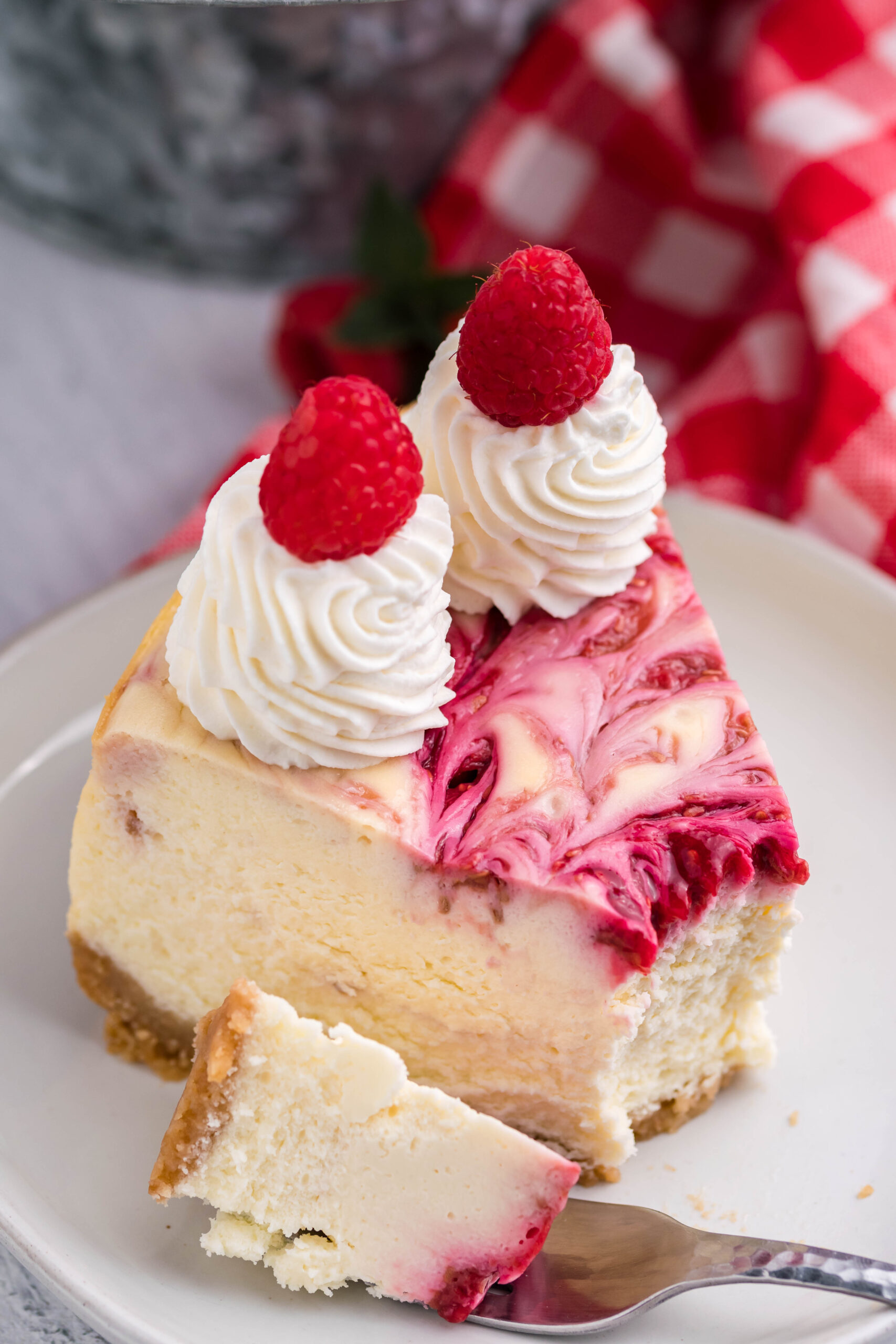 Raspberry Swirl Cheesecake slice on a white dish with a bite removed by a silver fork.