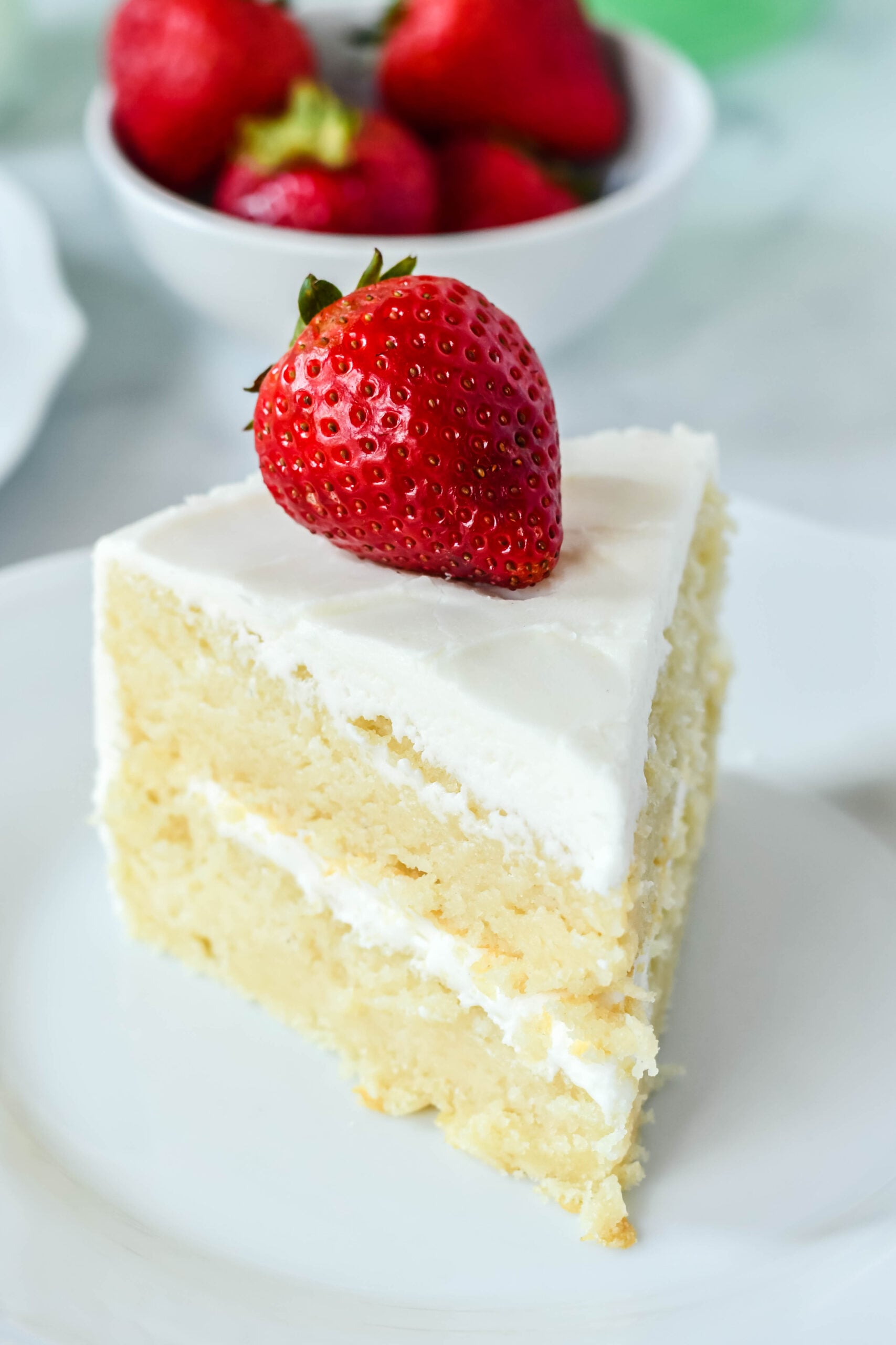 Up close view of a slice of Classic Vanilla Cake on a white plate garnished with a strawberry.