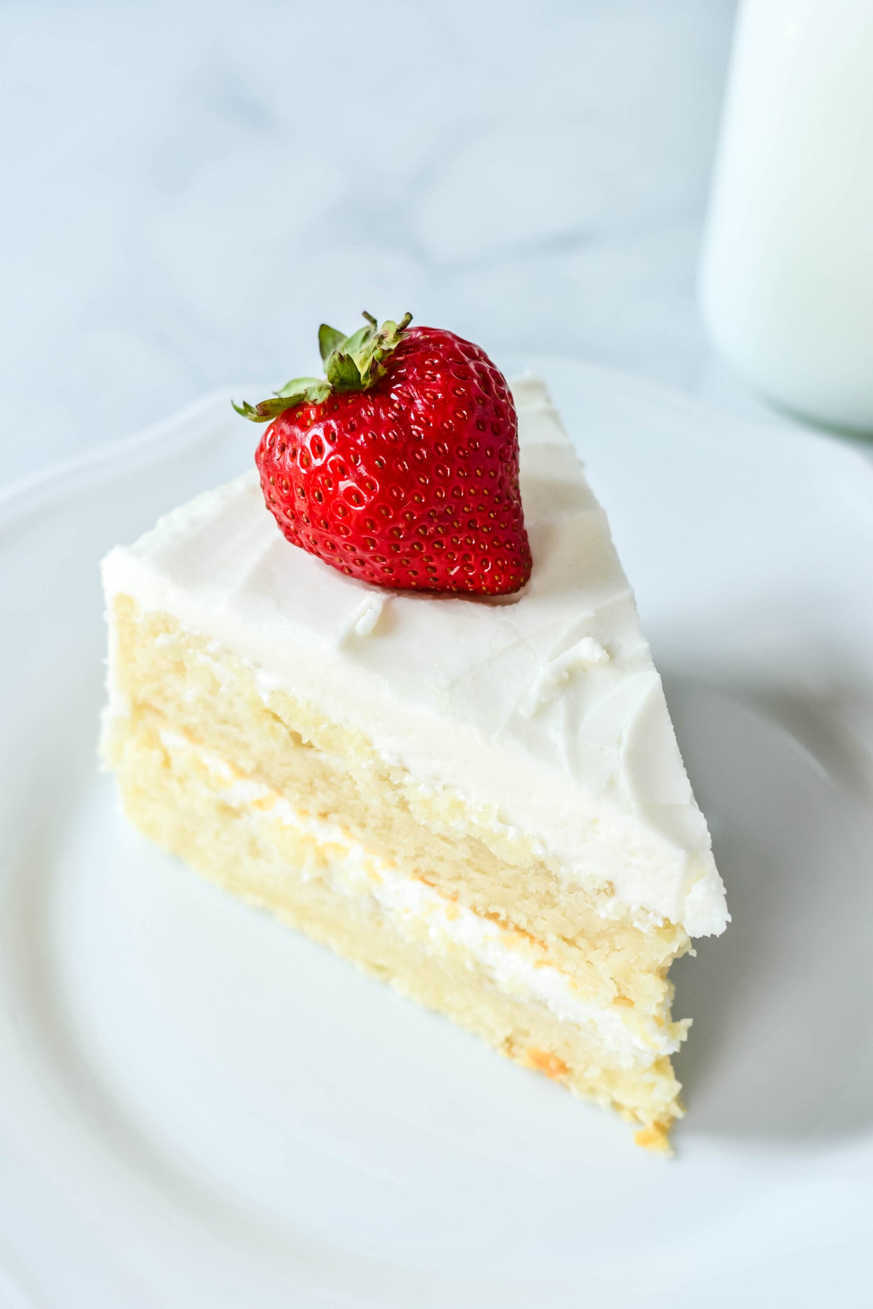 Up close view of a slice of Classic Vanilla Cake on a white plate garnished with a strawberry.
