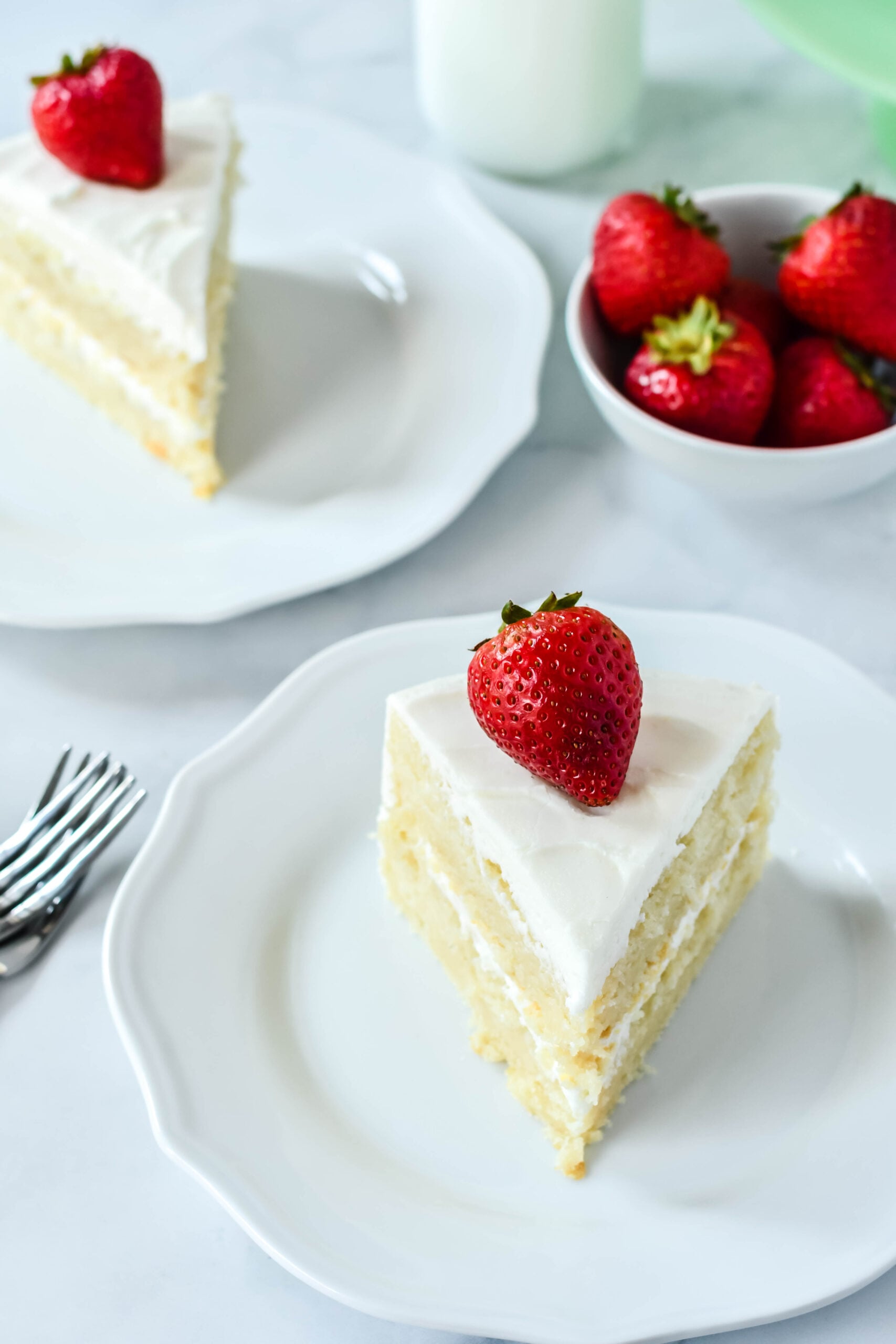 Front view of a slice of Classic Vanilla Cake on a white plate garnished with a strawberry.
