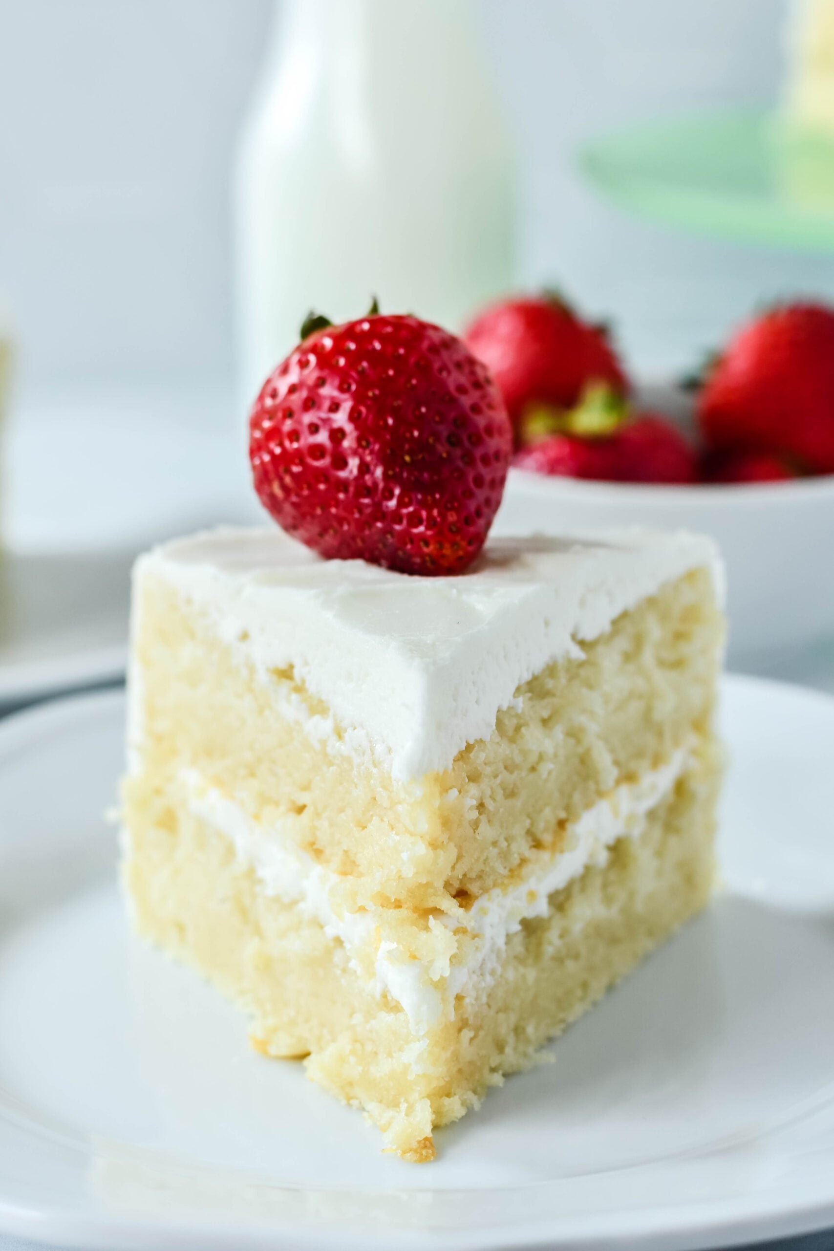 Front view of a slice of Classic Vanilla Cake on a white plate garnished with a strawberry.