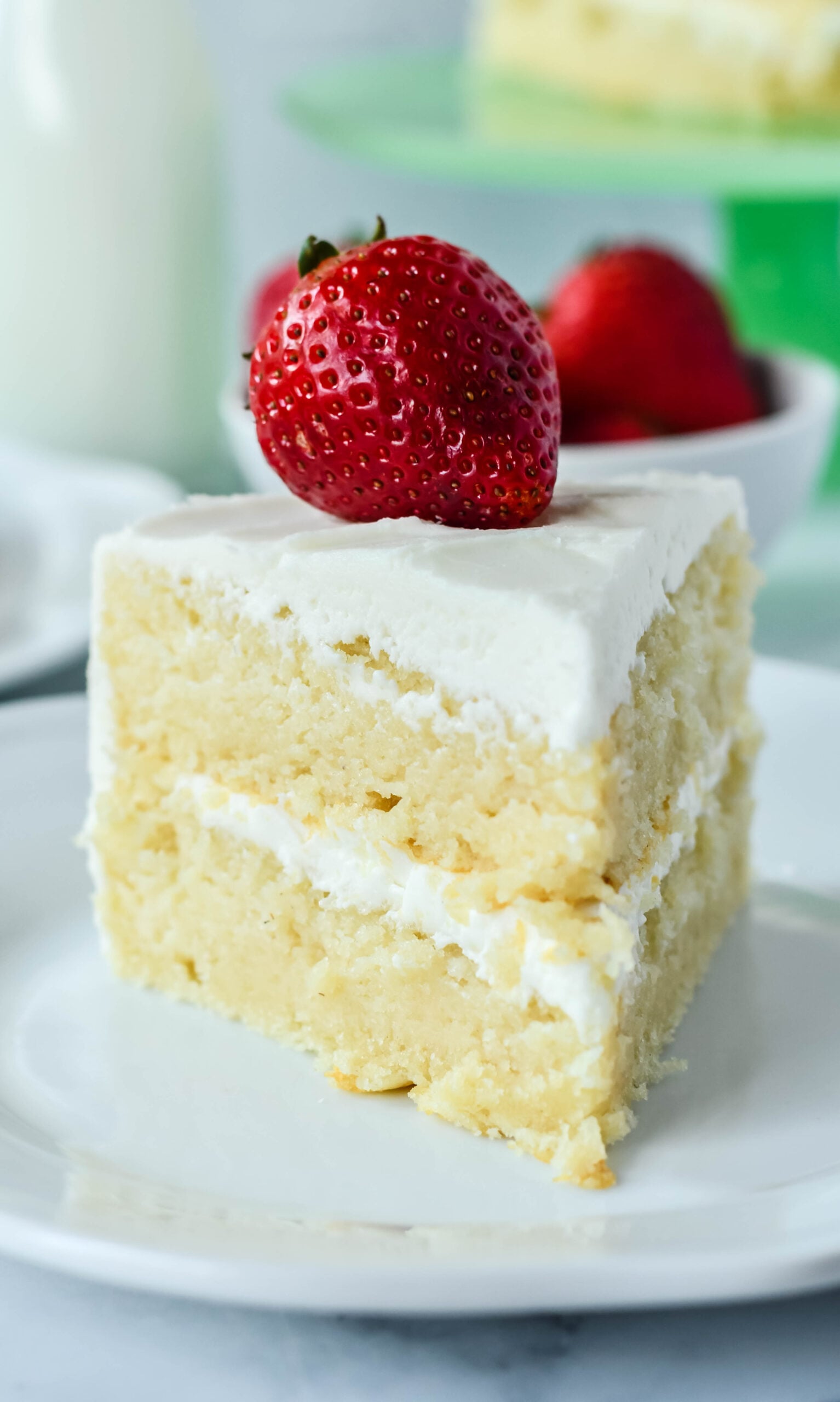 Front view of a slice of Classic Vanilla Cake on a white plate garnished with a strawberry.