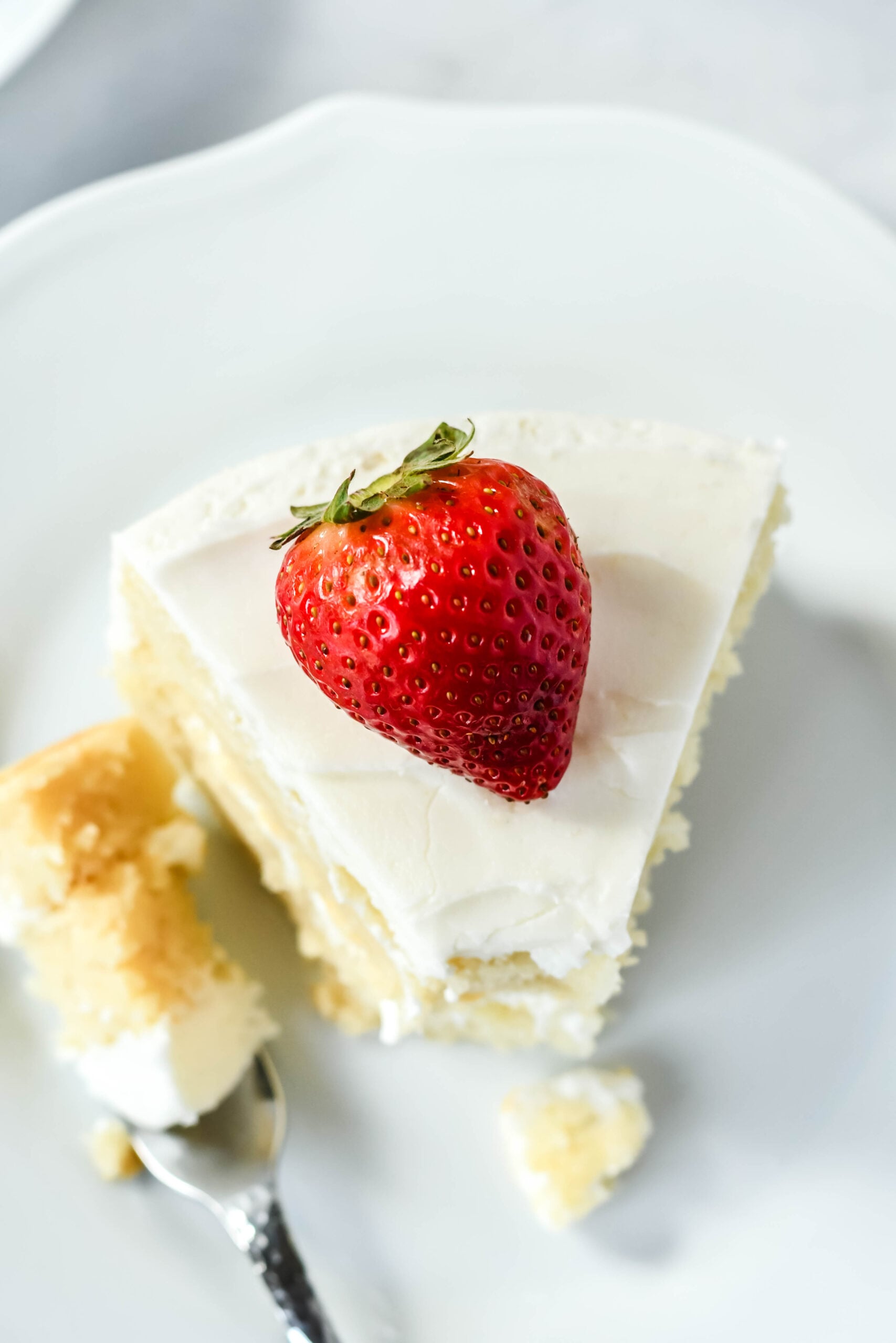 Overhead view of a slice of Classic Vanilla Cake on a white plate garnished with a strawberry with a bite removed.