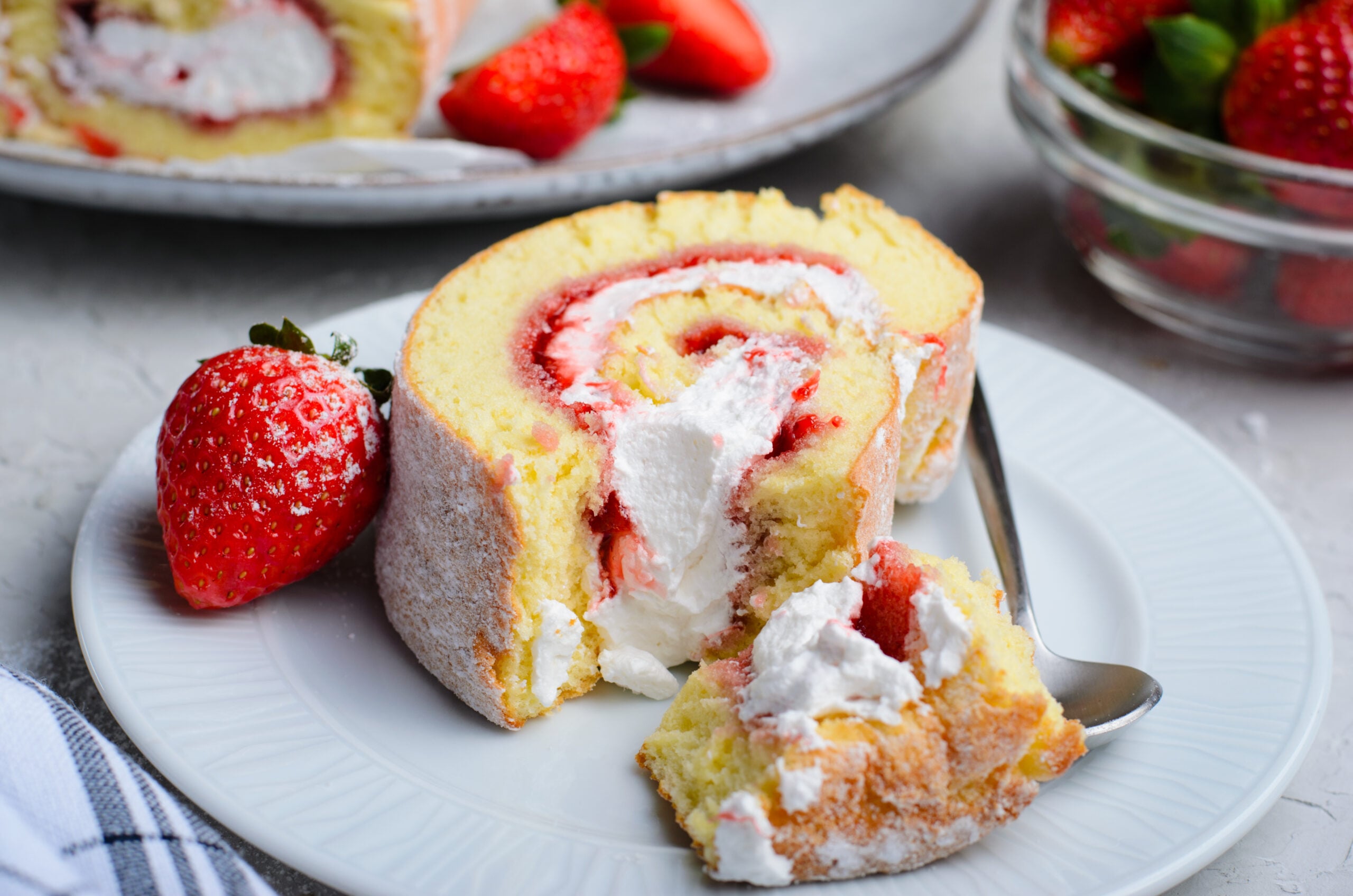 Front view of a slice of Strawberries & Cream Cake Roll with a bite removed
