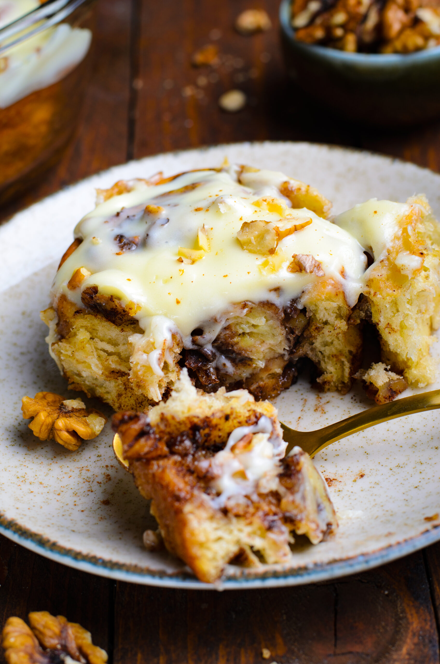 Front view of a Banana Nut Cinnamon Roll with a bite removed with a golden fork.