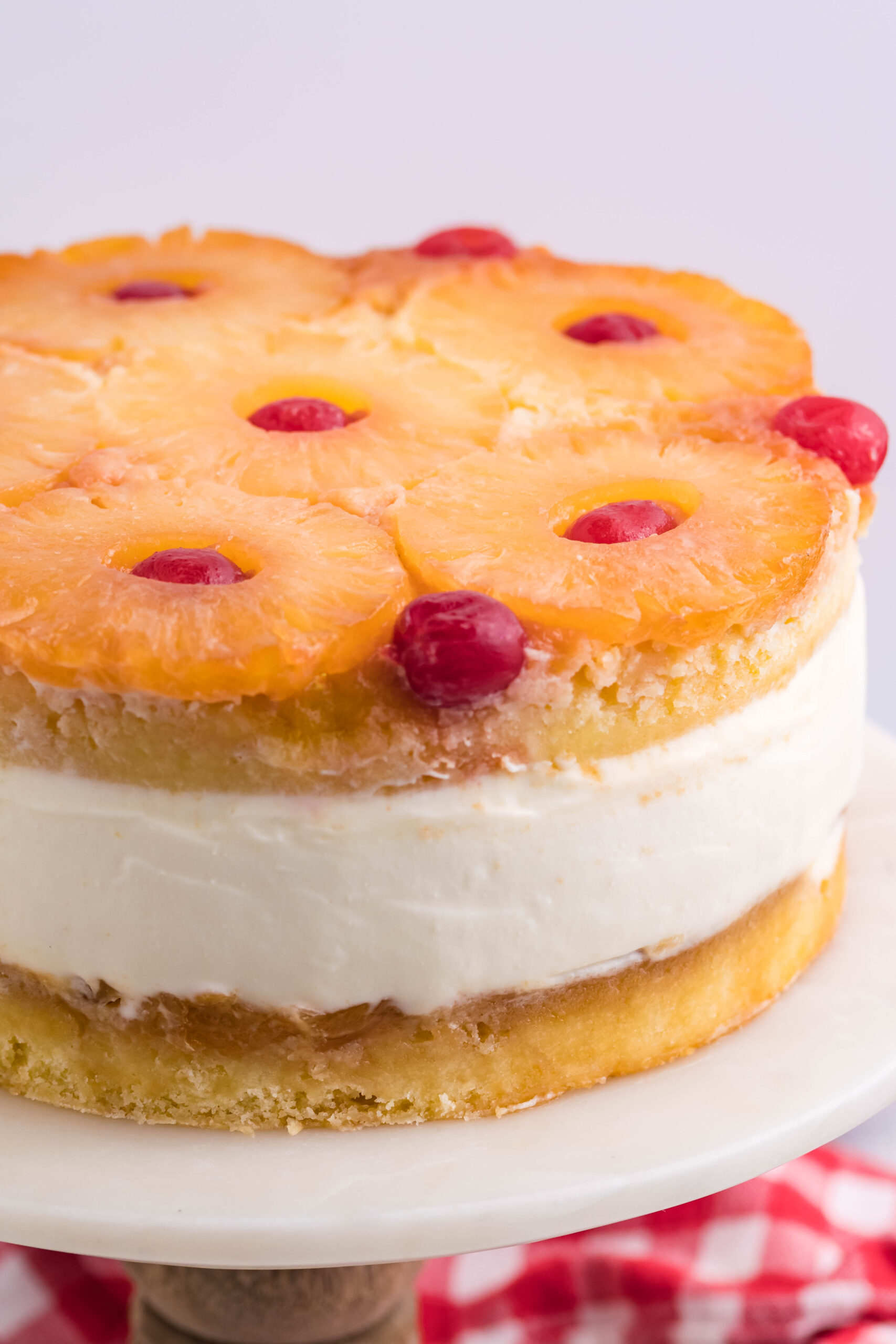 Up close view of Pineapple Upside Down Cheesecake Cake on a white and wooden cake stand.