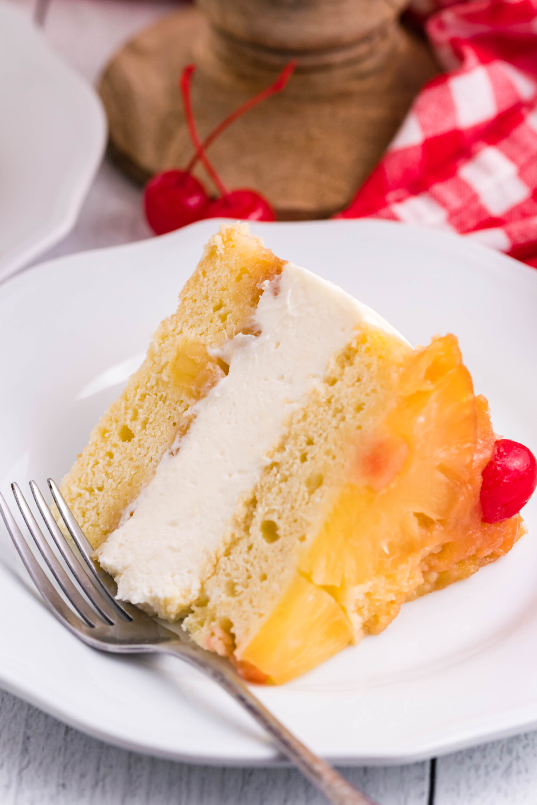 Front view of a slice of Pineapple Upside Down Cheesecake Cake served on a white plate with a silver fork.